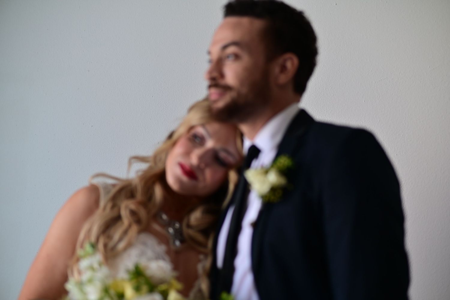 A happy couple in wedding attire share an intimate moment while holding a bouquet of white flowers.