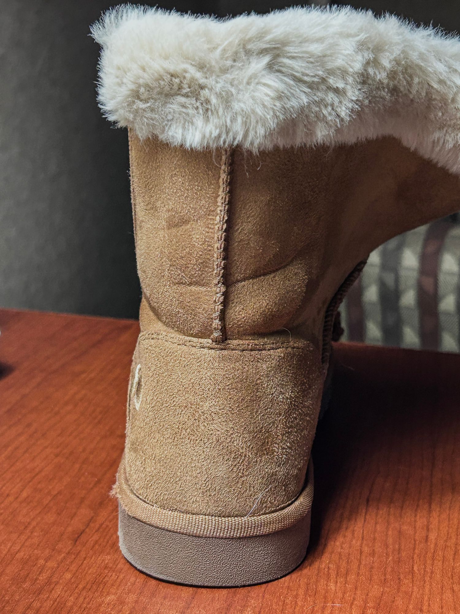 Tan suede boot with white fur trim sitting on wooden surface.
