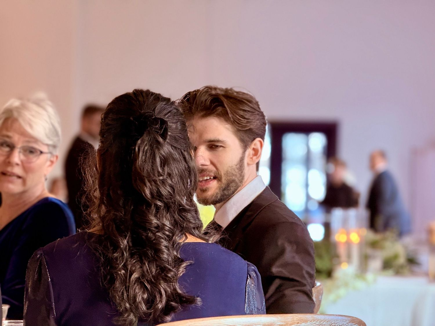 Groom in black tuxedo greeting guest at elegant wedding reception venue.