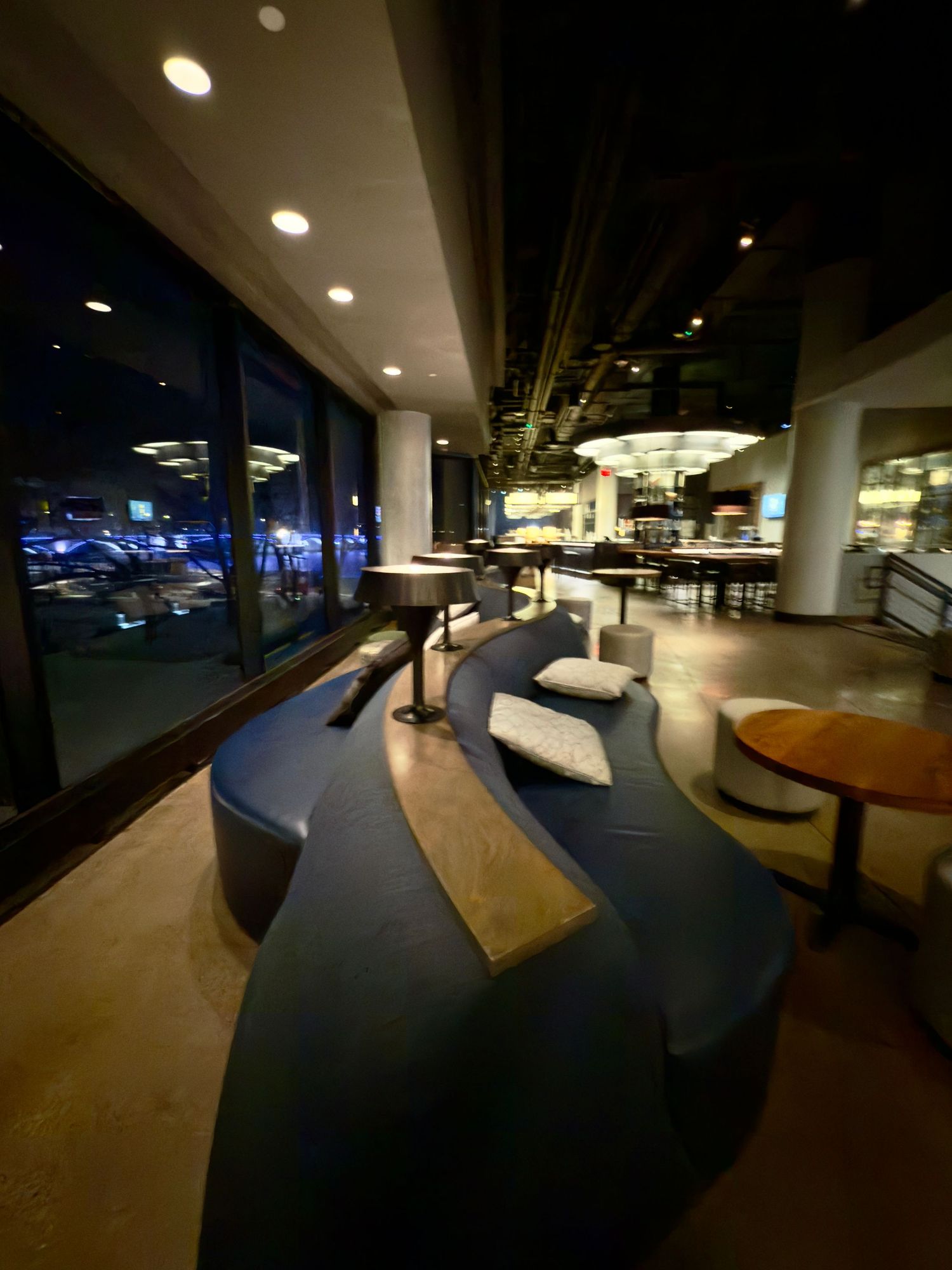 Modern office lounge area with curved seating and wooden tables illuminated by recessed lighting at night.