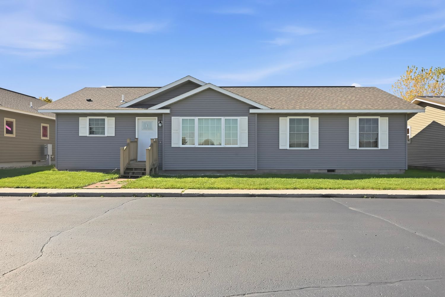Exterior view of residential homes with gray siding and landscaping under a bright blue sky.
