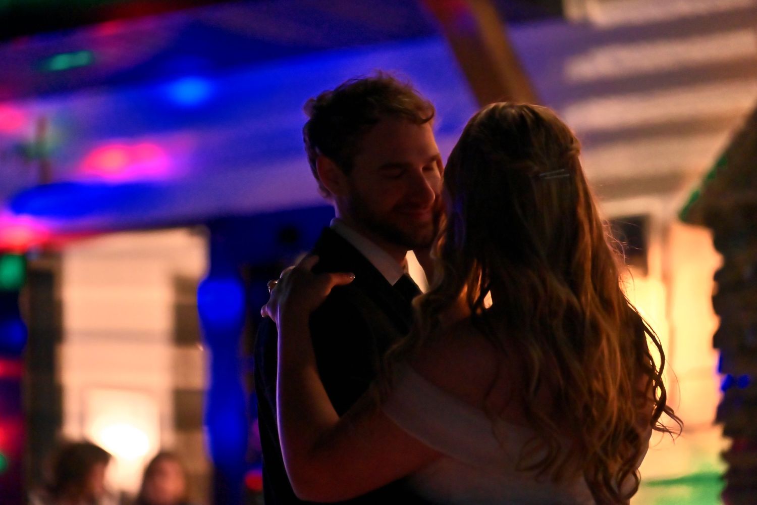 Couple sharing a romantic first dance at a wedding reception with colorful ambient lighting.