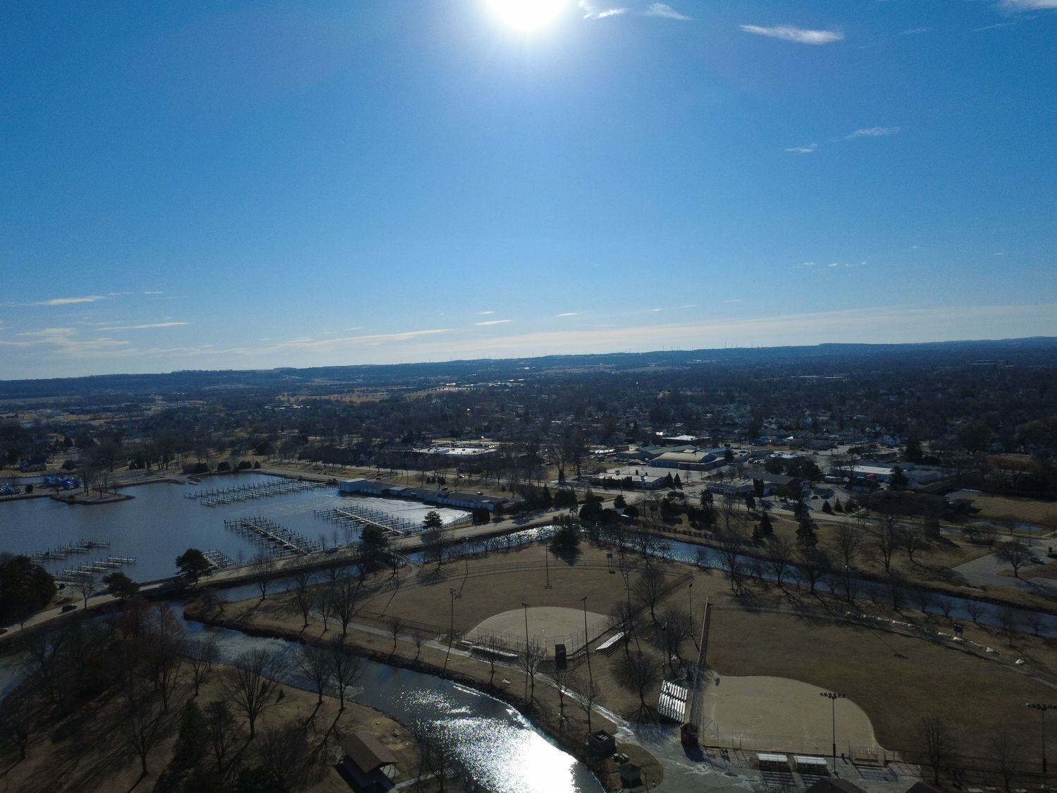 Aerial view of a sunny winter landscape with frozen lakes and sports fields surrounded by trees and buildings.