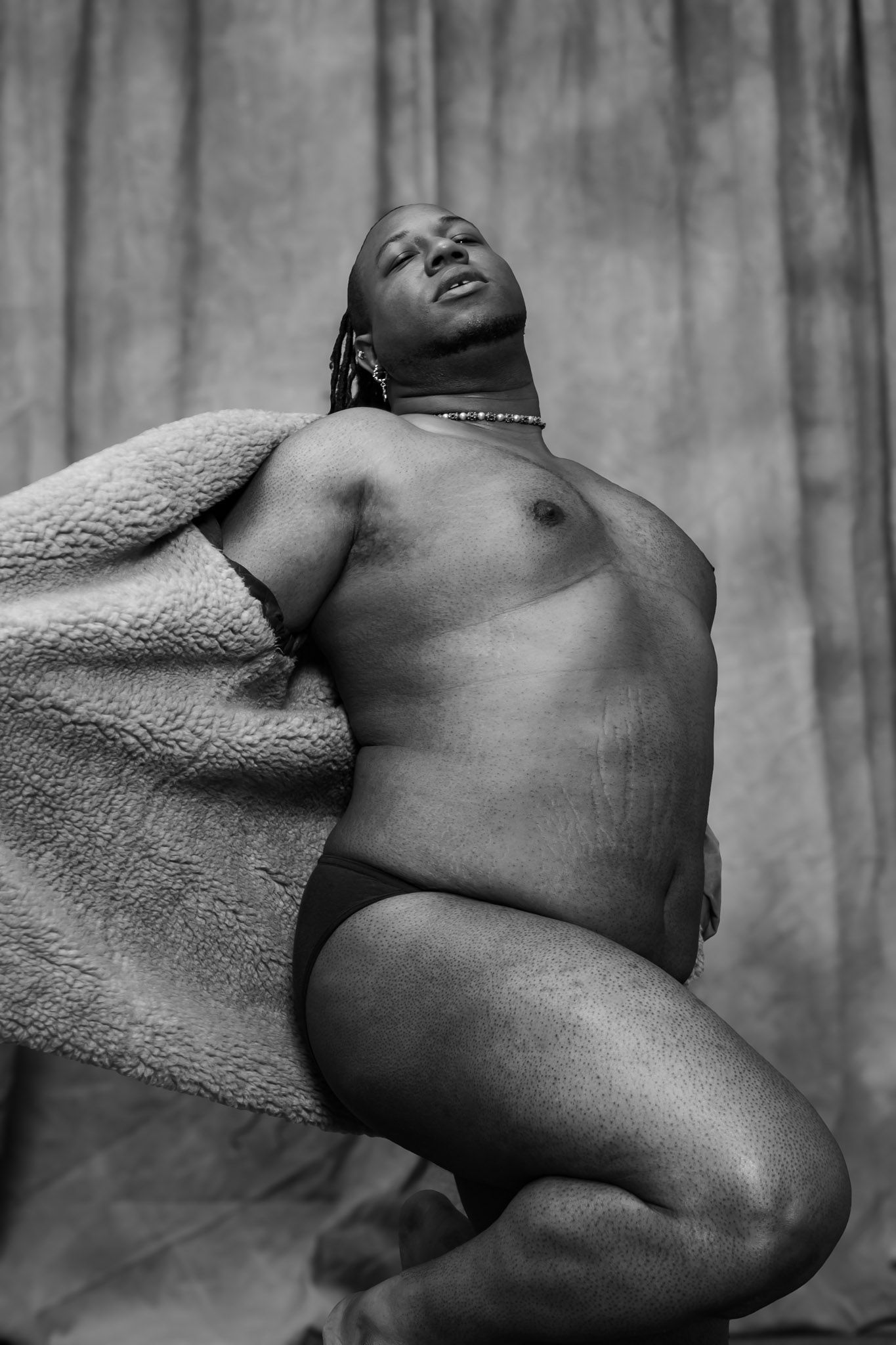 Black and white artistic nude study showing reclining figure against textured backdrop with dramatic shadows.