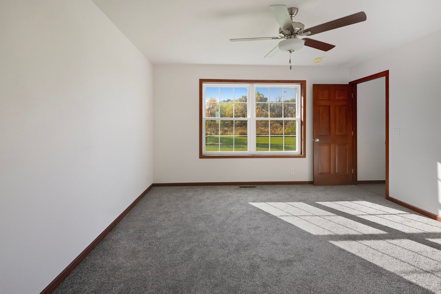 Empty room with gray carpet, white walls, and large windows letting in natural light.