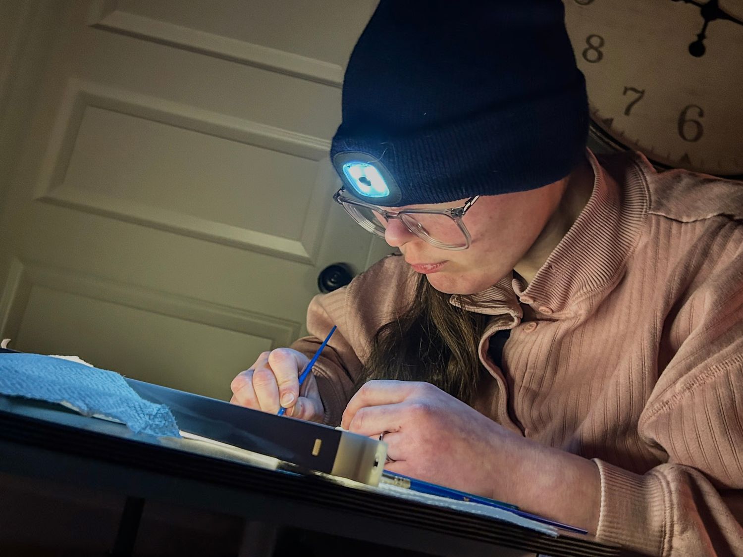 Person wearing glasses working intently on a detailed project under focused lighting.