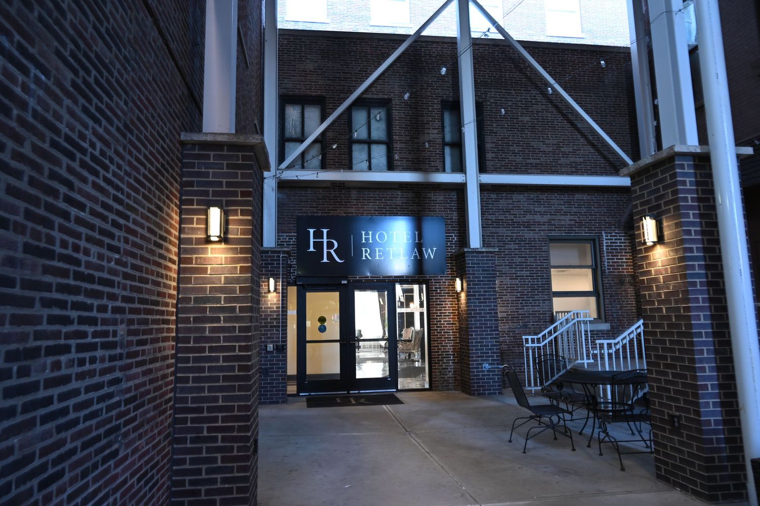 Exterior entrance of a brick building with glass doors and wall sconces illuminated at dusk.
