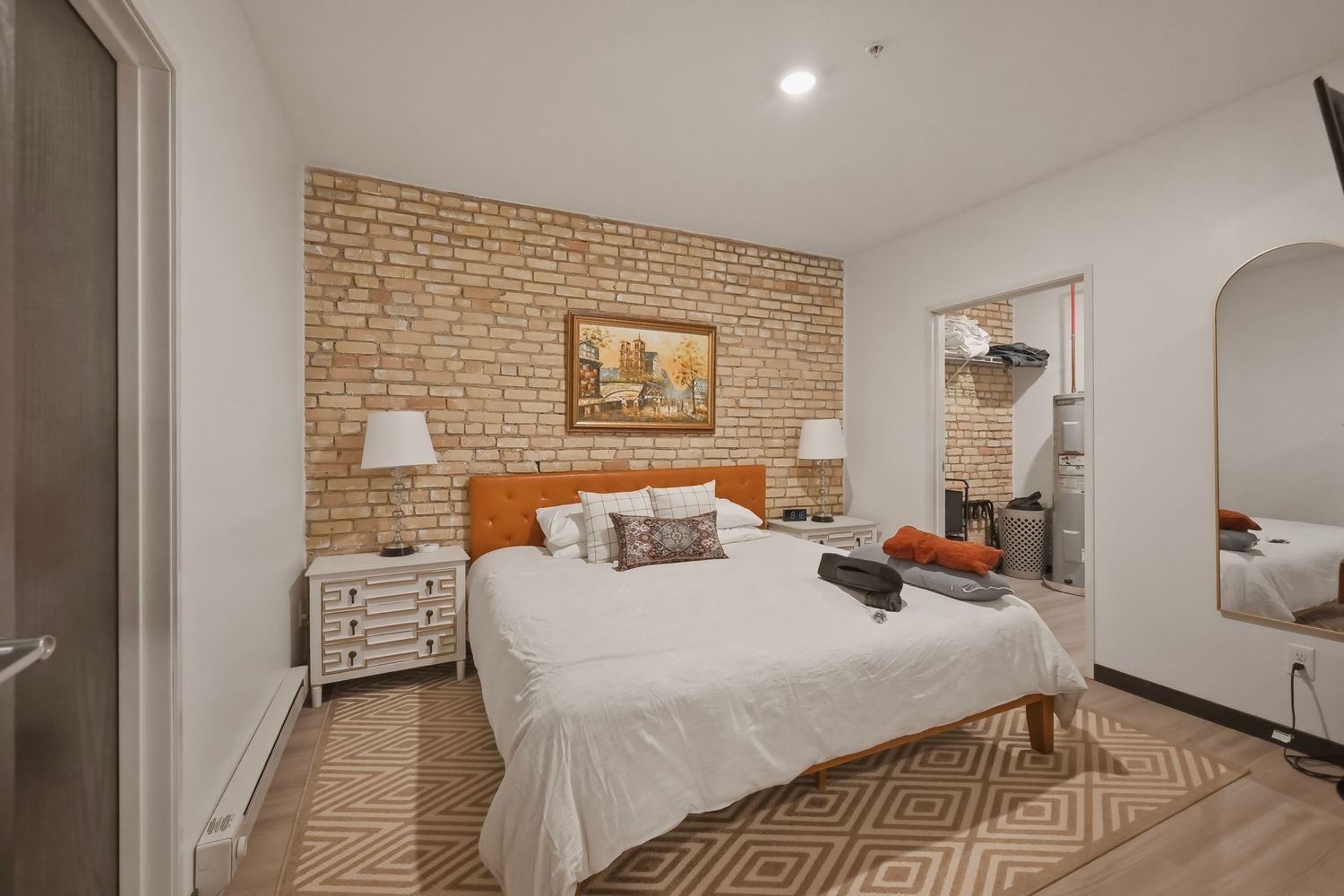 Modern bedroom with exposed brick wall, white bedding, geometric rug, and rustic decor elements.