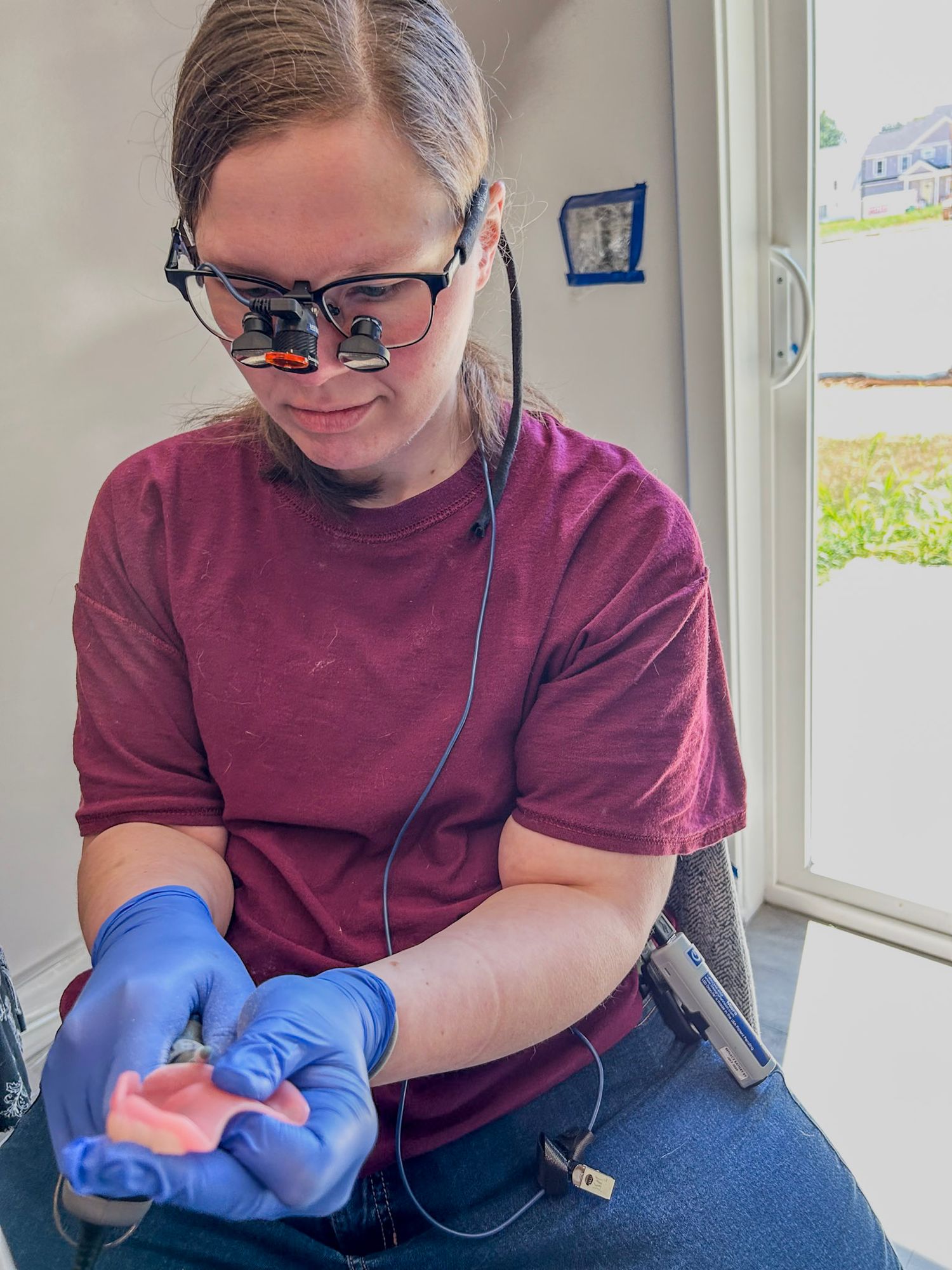 Person wearing burgundy shirt and blue gloves working at a desk.