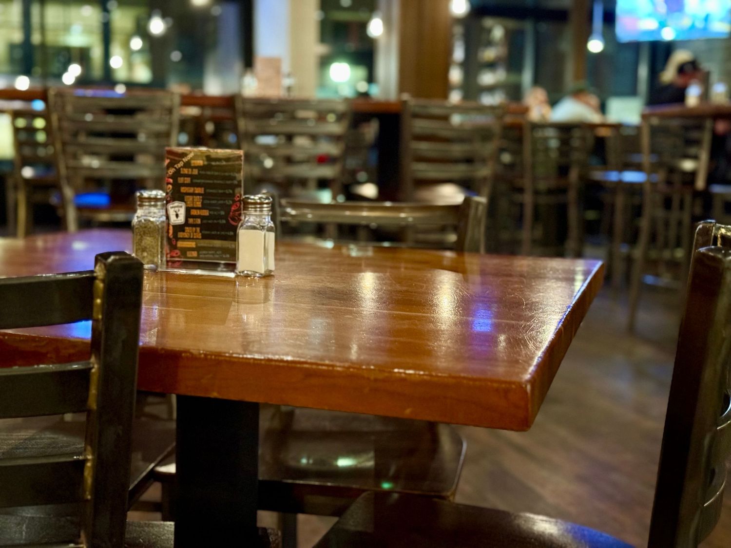 Wooden dining tables and chairs arranged in a restaurant interior with warm lighting and modern decor.