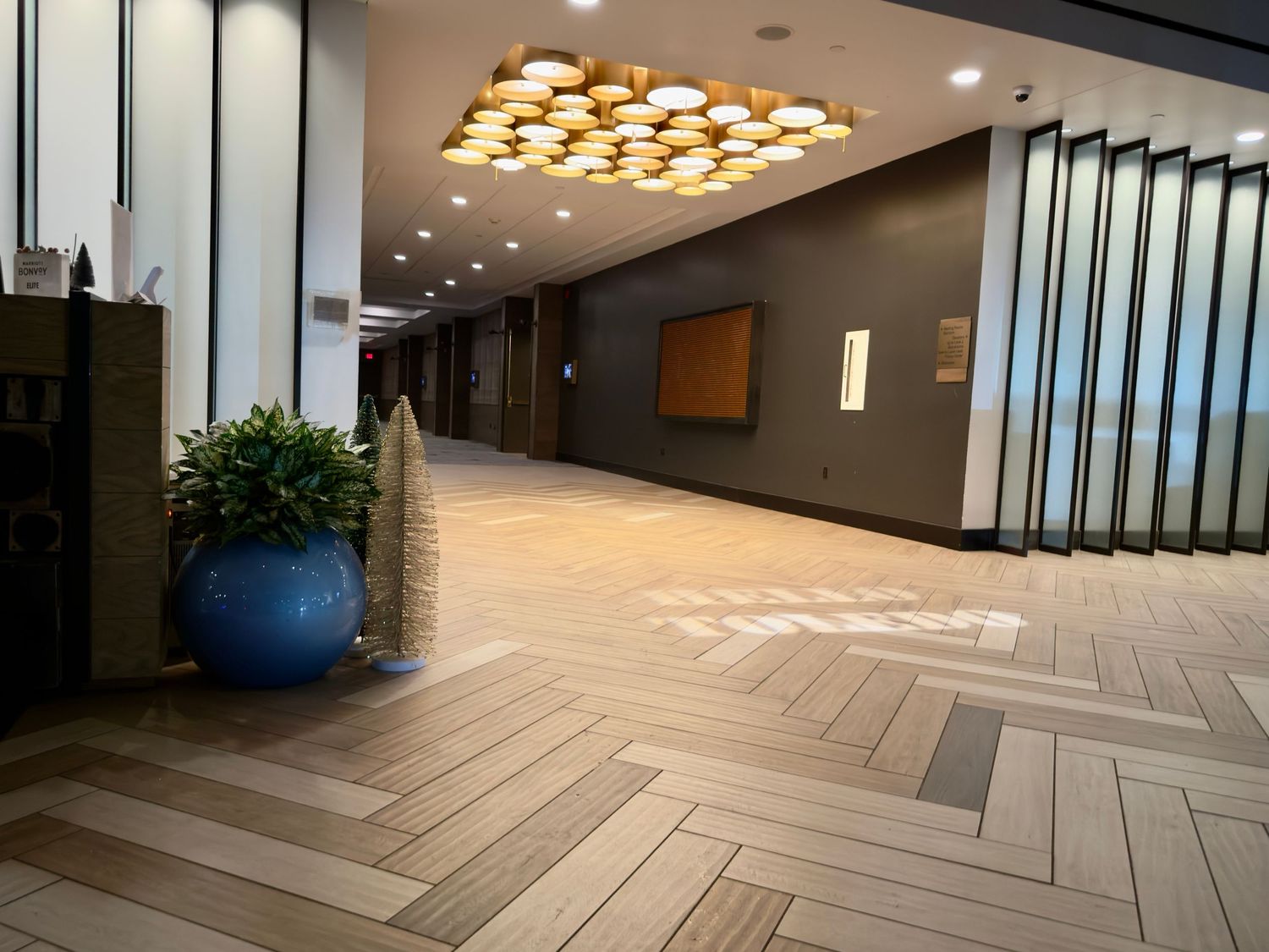 Modern office hallway with herringbone pattern flooring, recessed lighting, and contemporary architectural design.