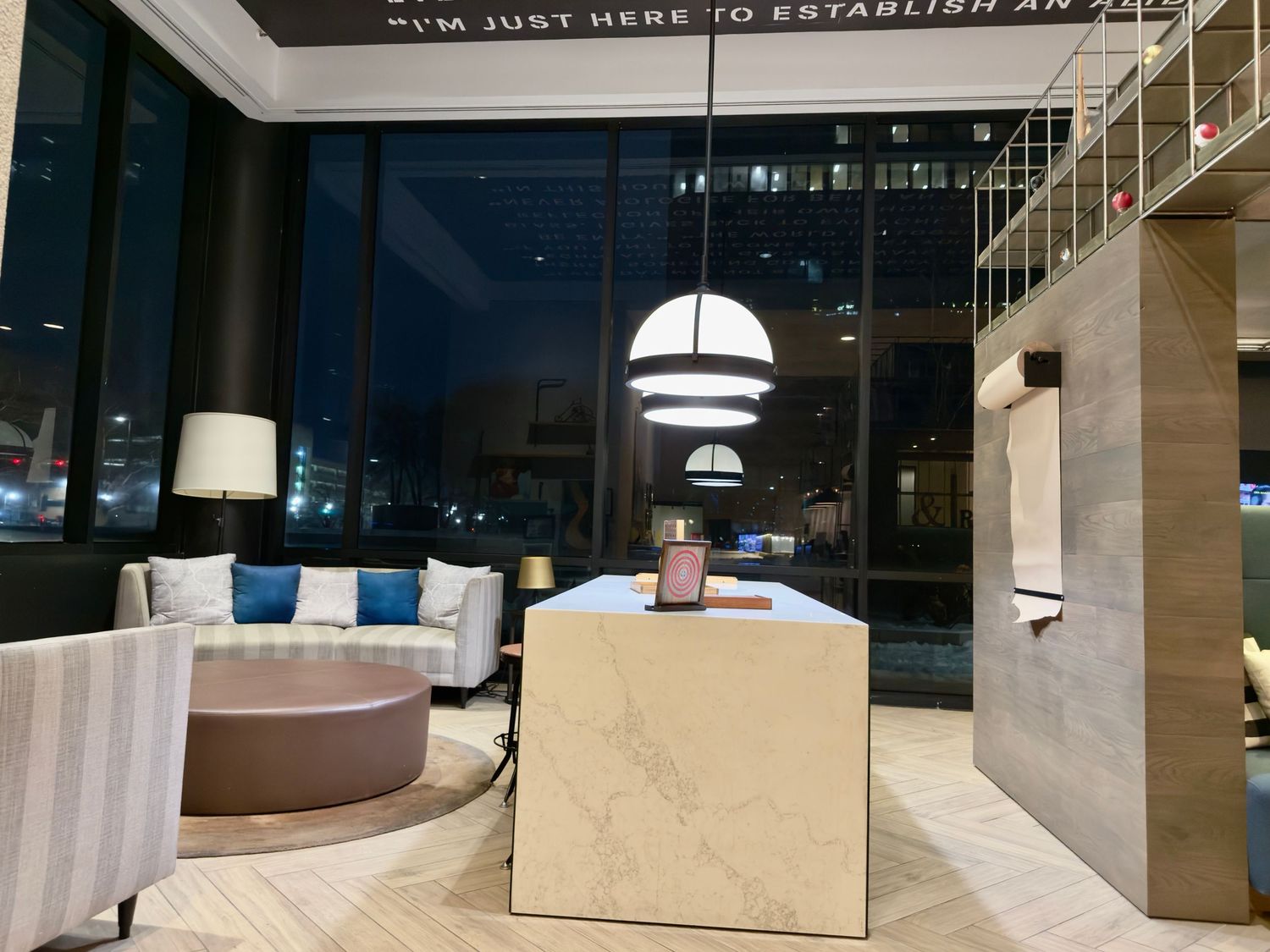 Modern hotel lobby interior with curved seating, white cube tables and hanging dome pendant lights at night.