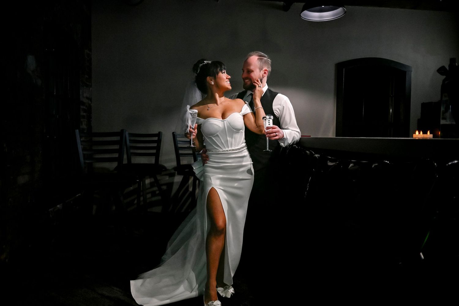 Couple share a romantic first look holding champagne glasses in a dimly lit wedding reception venue. By https://www.ClassicVibeWeddings.com