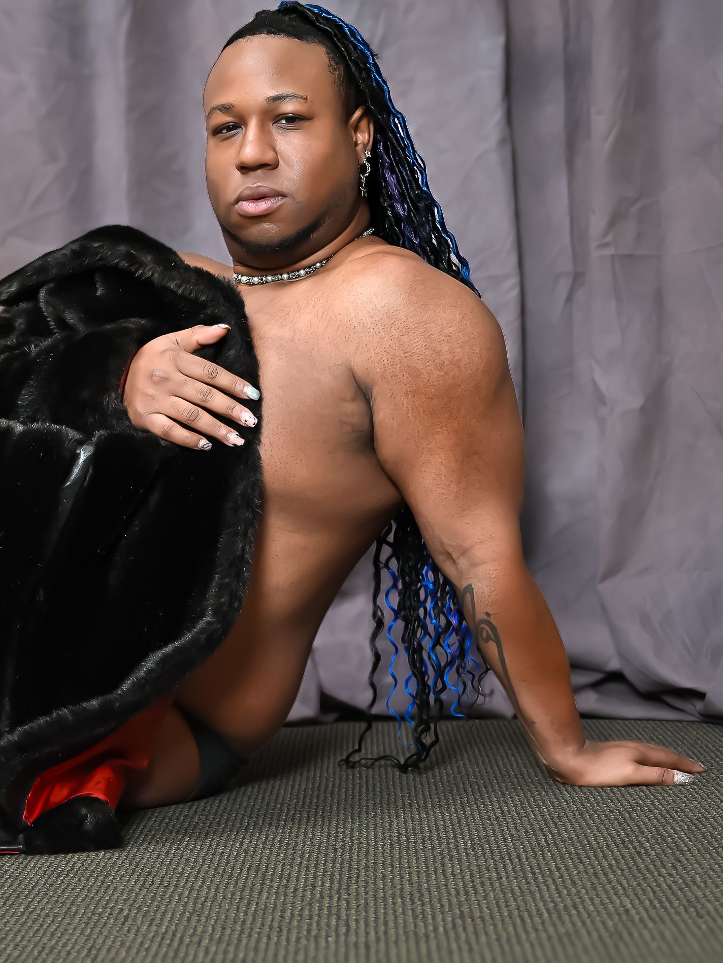 A person with blue braids poses on the floor against a grey backdrop in a creative photo series.