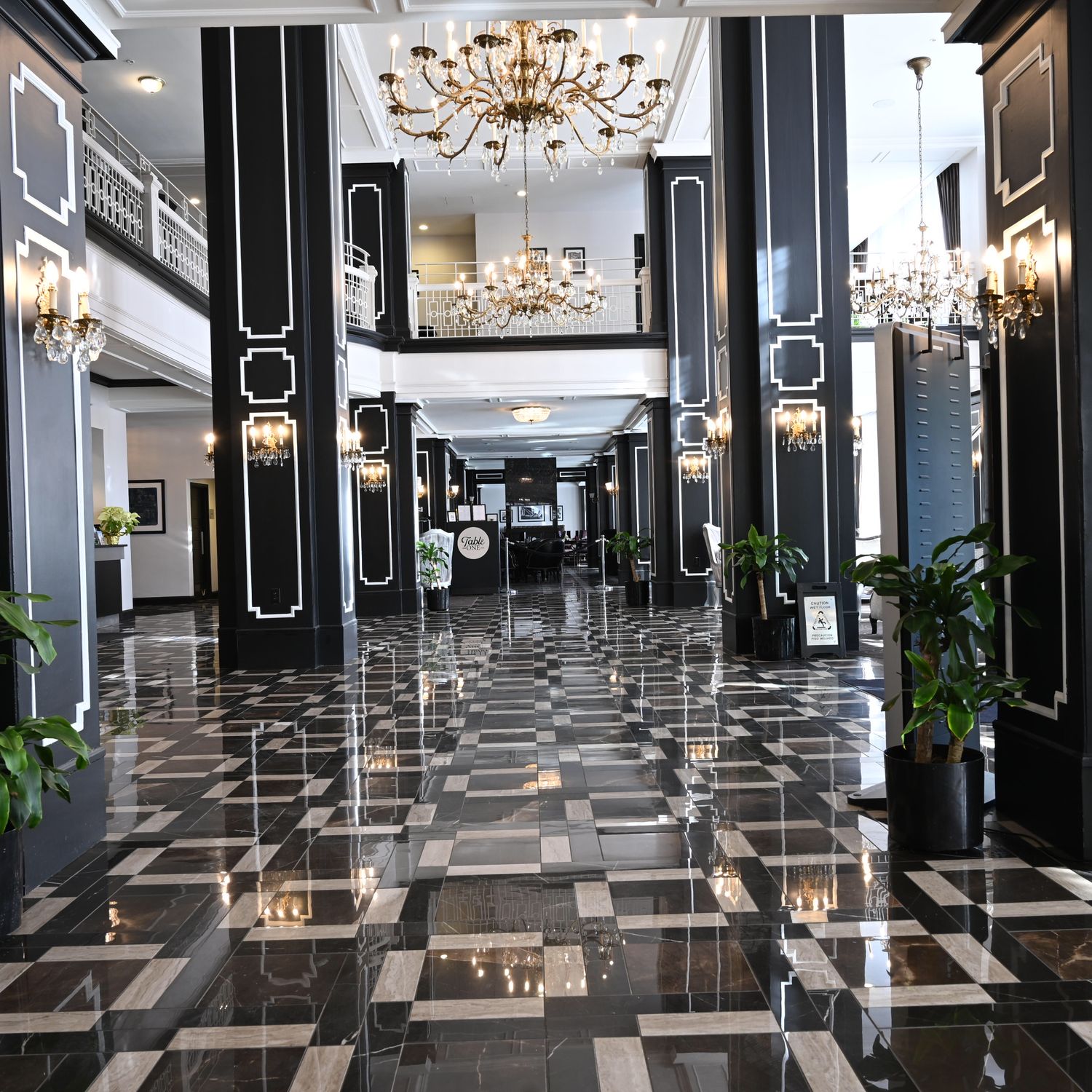 Elegant hotel lobby with black and white checkered marble floors, mirrored walls, and crystal chandeliers.