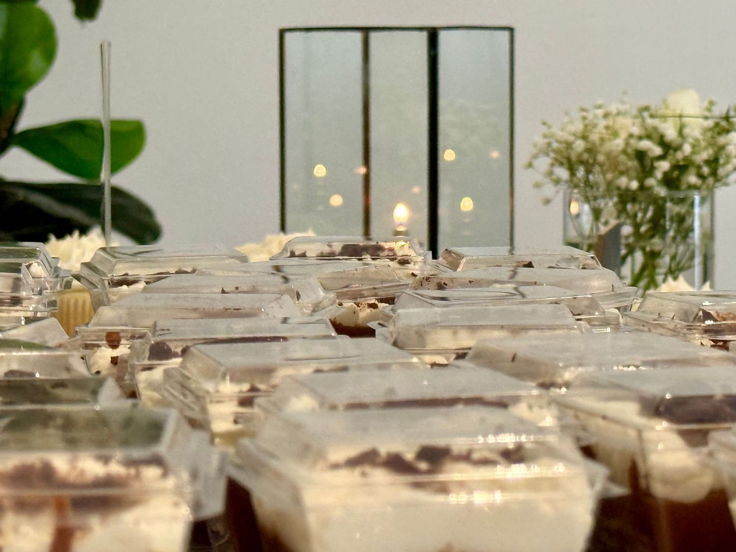 Rows of plastic containers filled with layered chocolate desserts displayed on a table with candles and flowers.