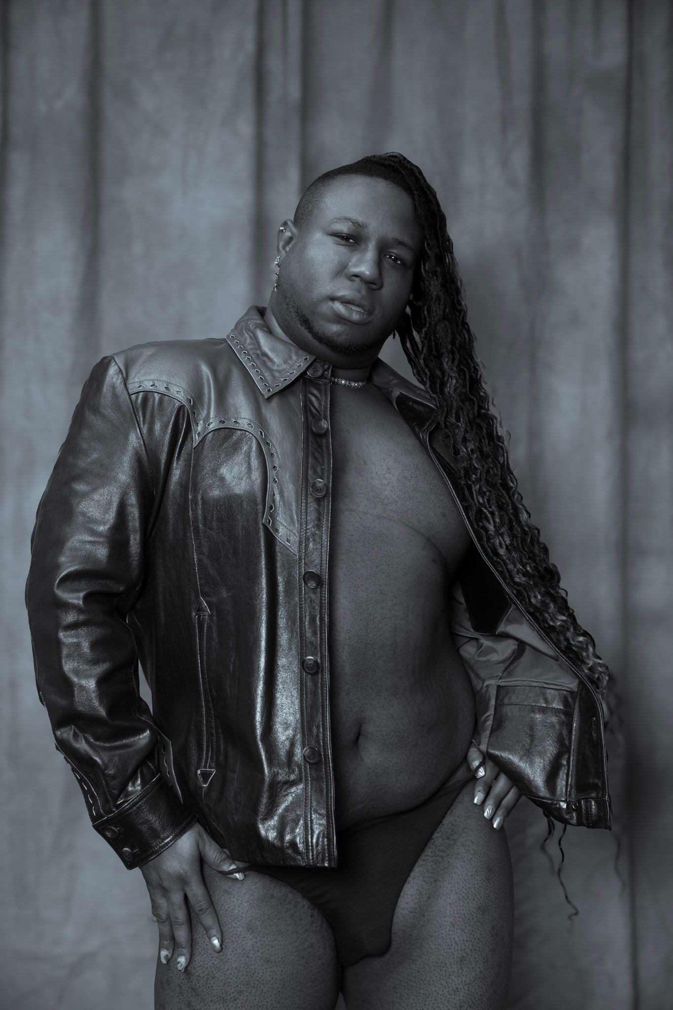Black and white artistic portrait showing a figure in a leather jacket posing against a textured backdrop.