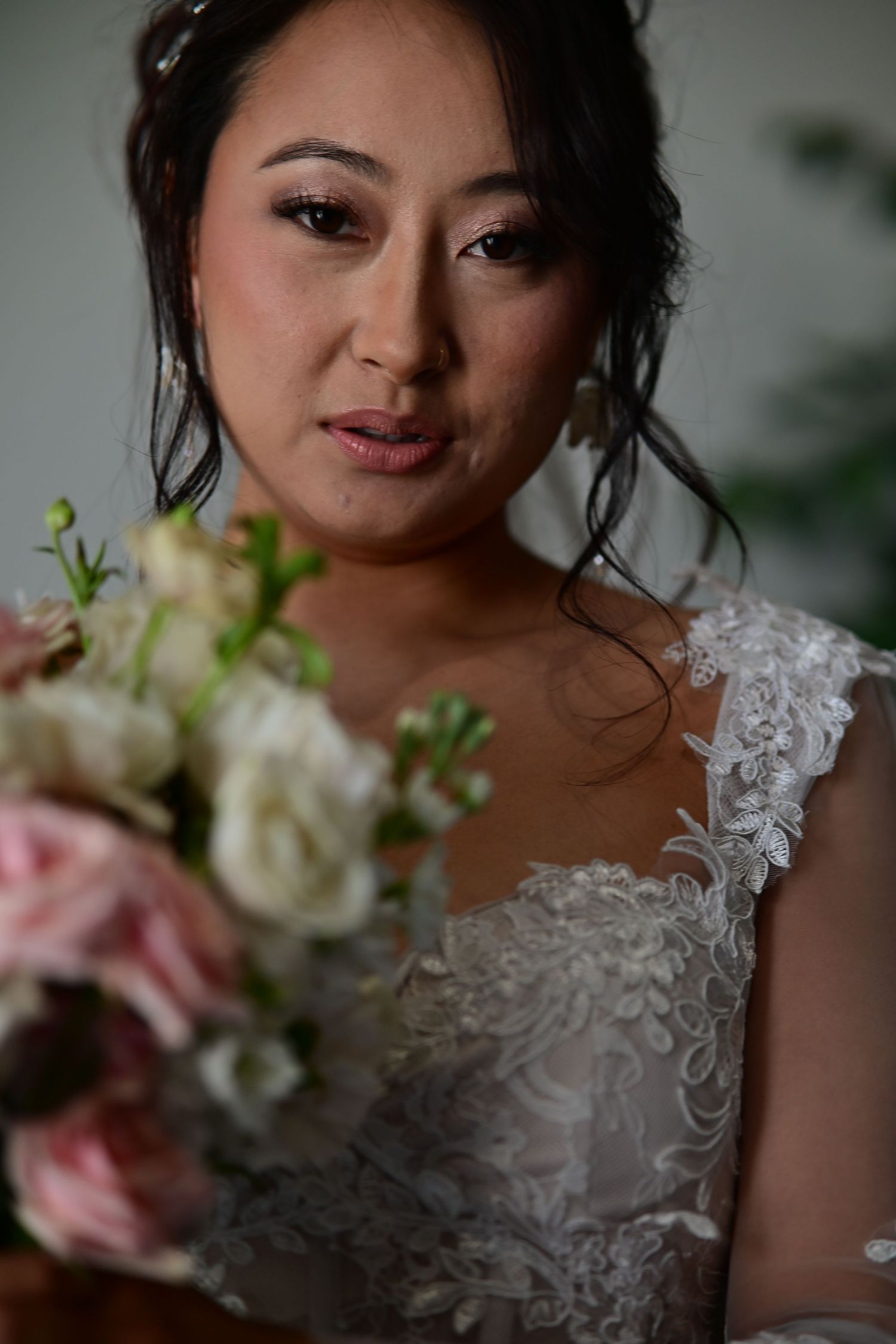 A bride in a delicate lace wedding dress poses with a soft pink and white floral bouquet in a romantic portrait series.