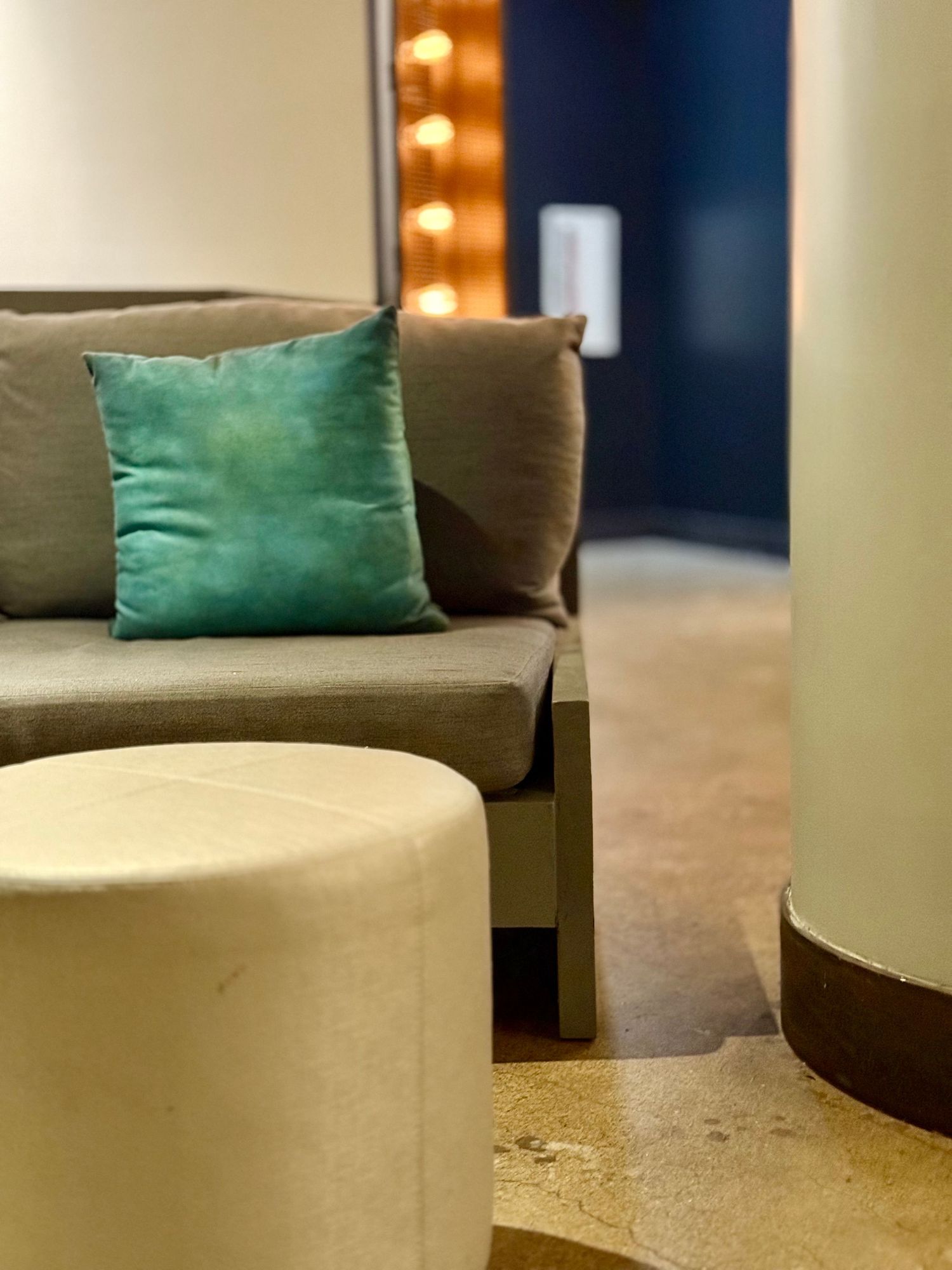 Modern curved sofa with emerald green velvet throw pillow against dark blue wall in contemporary living space.