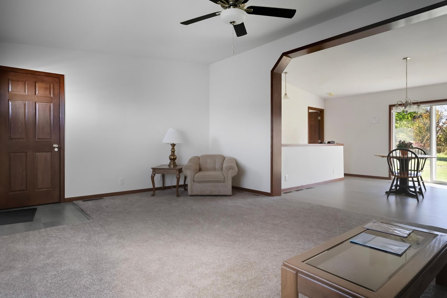 Empty living room interior with white walls, brown doors, and a ceiling fan in a residential home.
