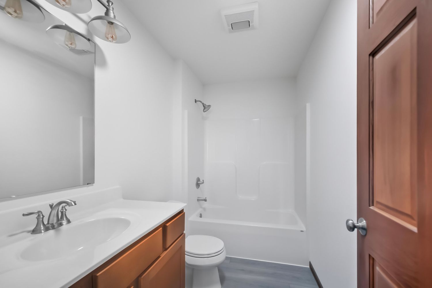 White bathroom interior with modern fixtures and wood door showing partial vanity and ceiling.