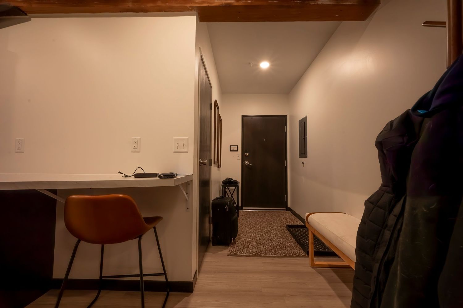 Dimly lit modern apartment hallway with white walls, hardwood floors, and recessed lighting creating a minimalist ambiance.