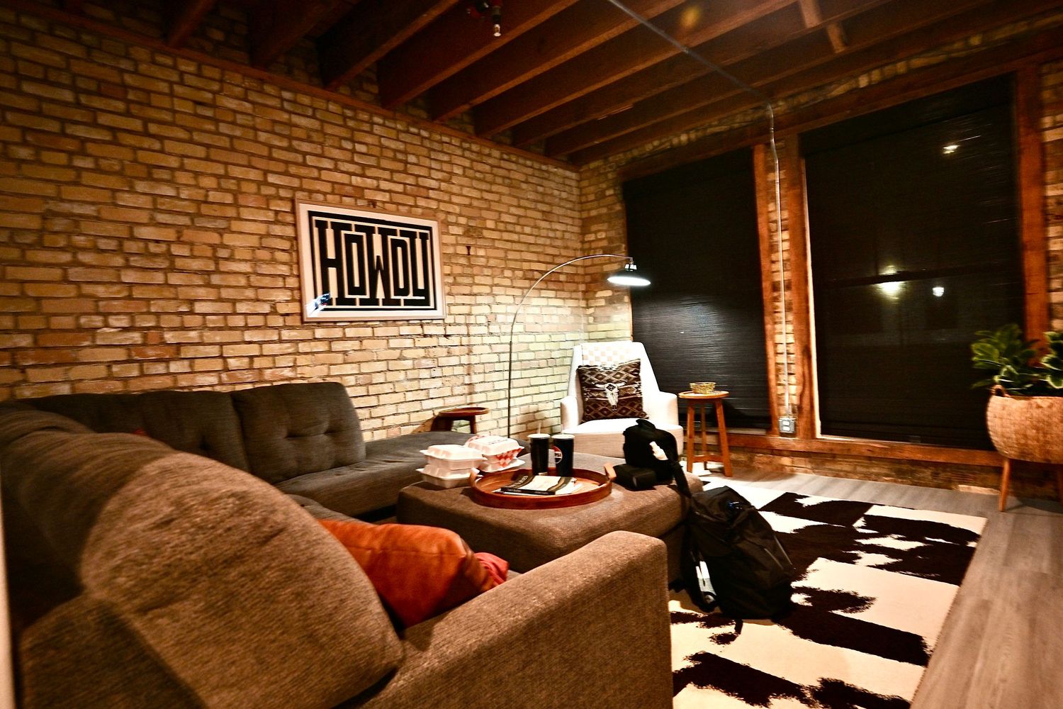 Modern industrial living room with exposed brick wall, cozy sectional sofa, and black and white cowhide rug.