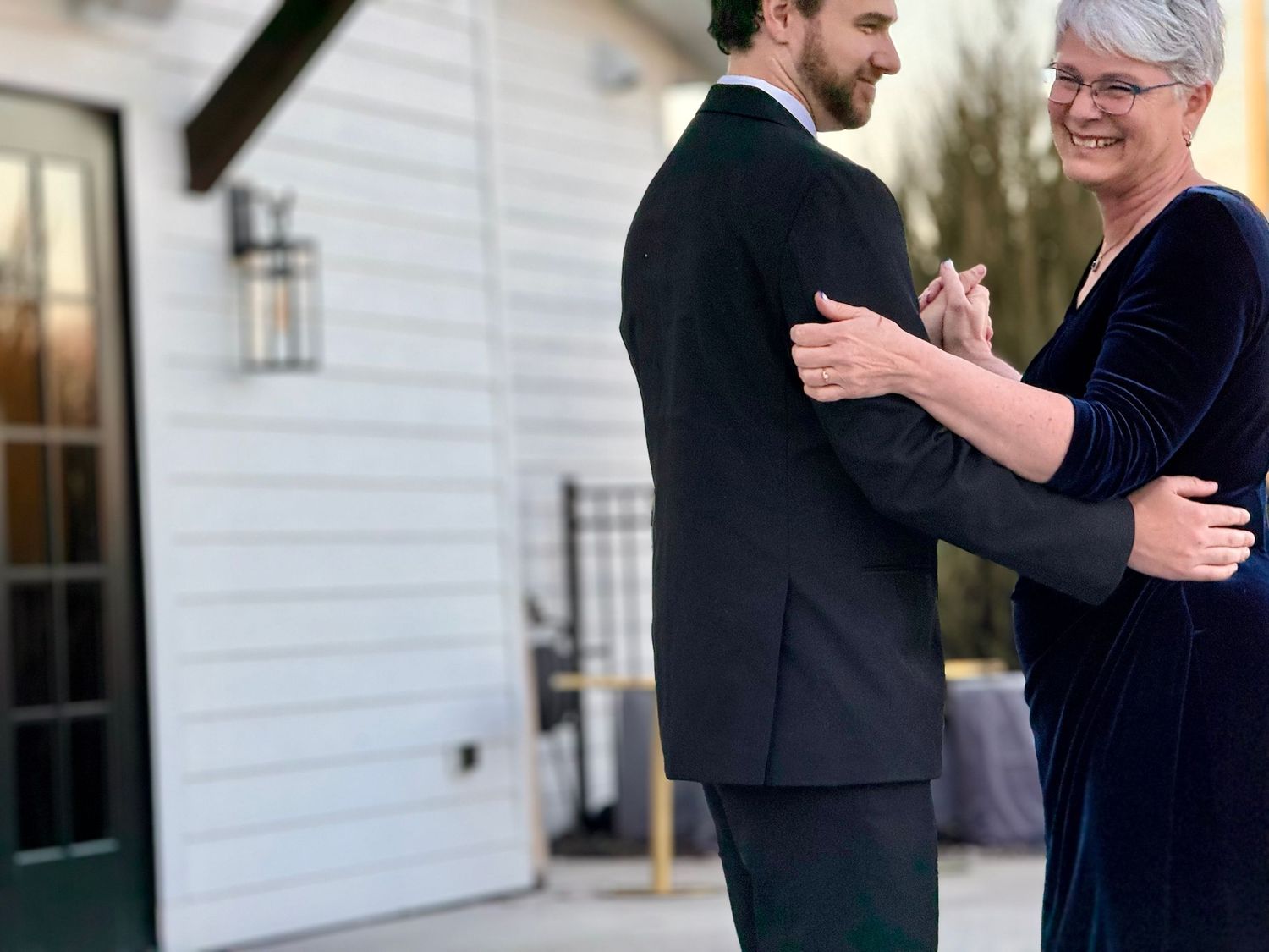 Couple dancing outdoors near a white building at dusk, woman in blue velvet dress and man in dark suit.