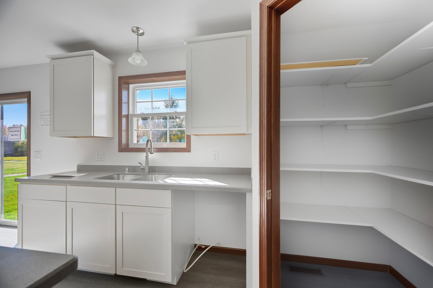 Modern white kitchen with stainless sink and adjacent pantry featuring empty white shelving.