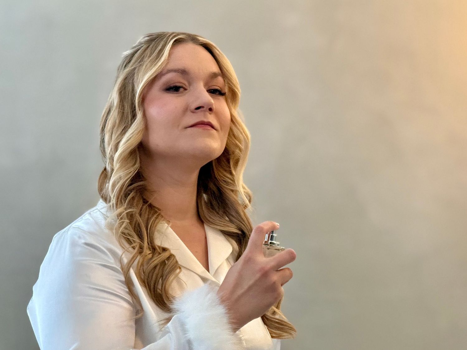 Young blonde woman in white blouse holding a decorative ring, posing against a gray background.