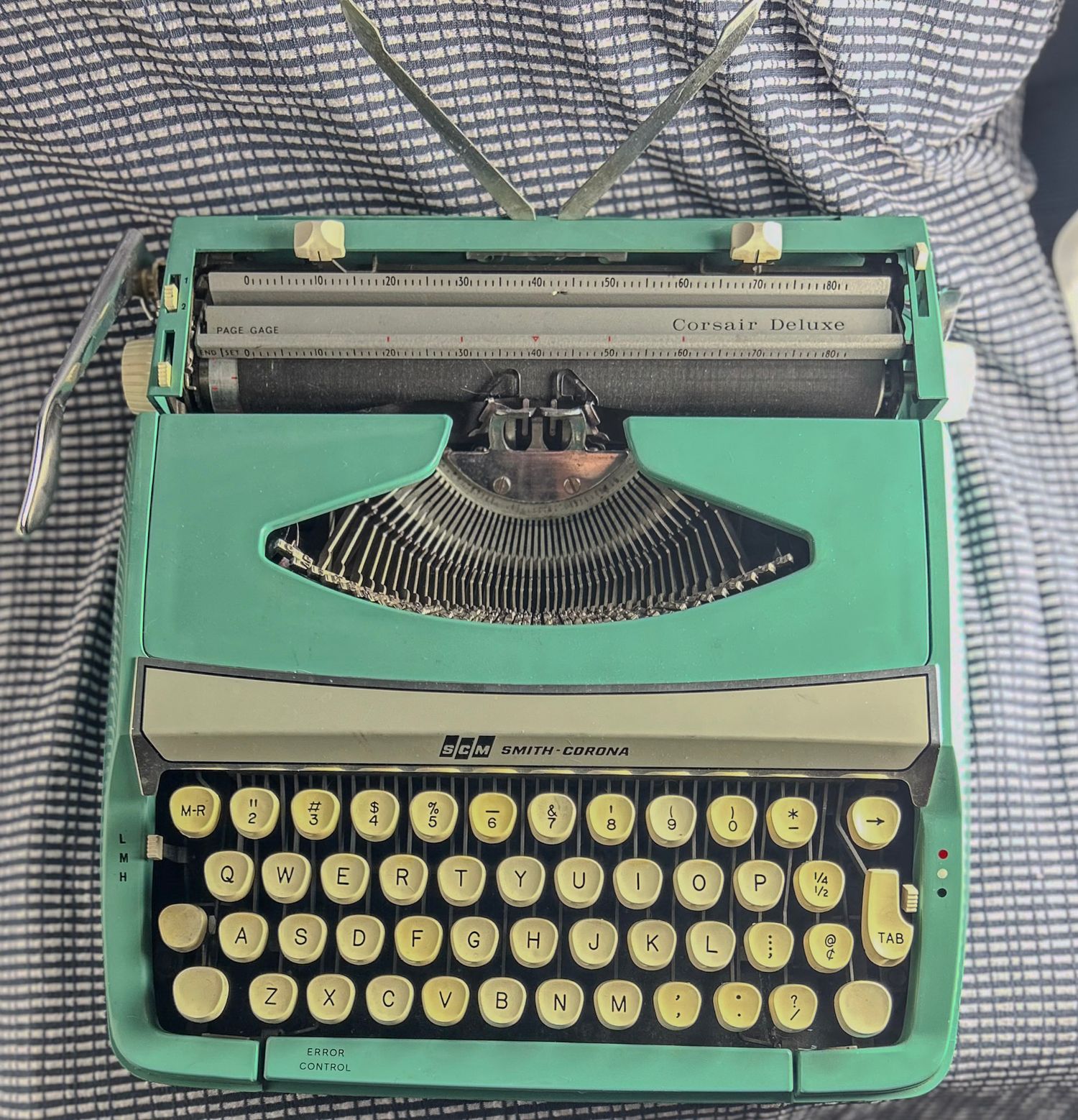 Retro mint green portable typewriter displayed on a checkered fabric surface.