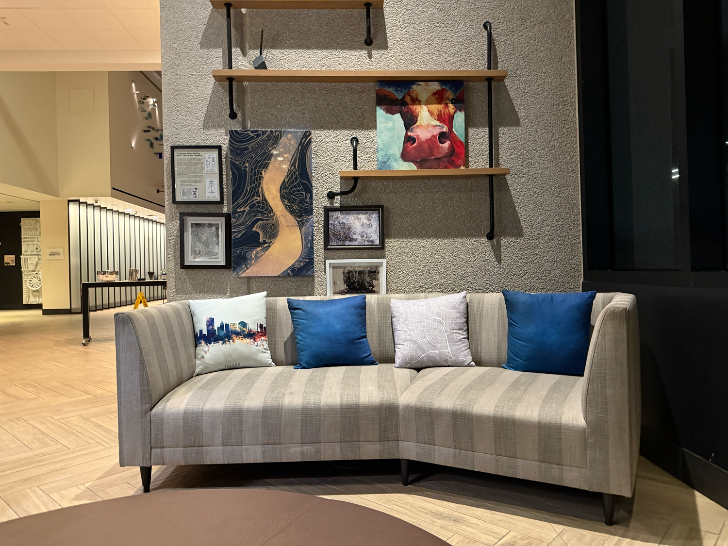 A modern living room features a gray sectional sofa with blue accent pillows and floating shelves on the wall.