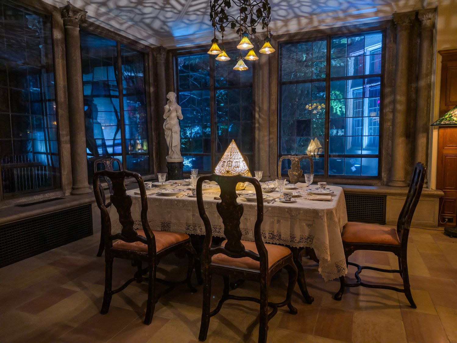 Elegant dining room with ornate chandeliers and dark wood furniture in dim evening lighting.