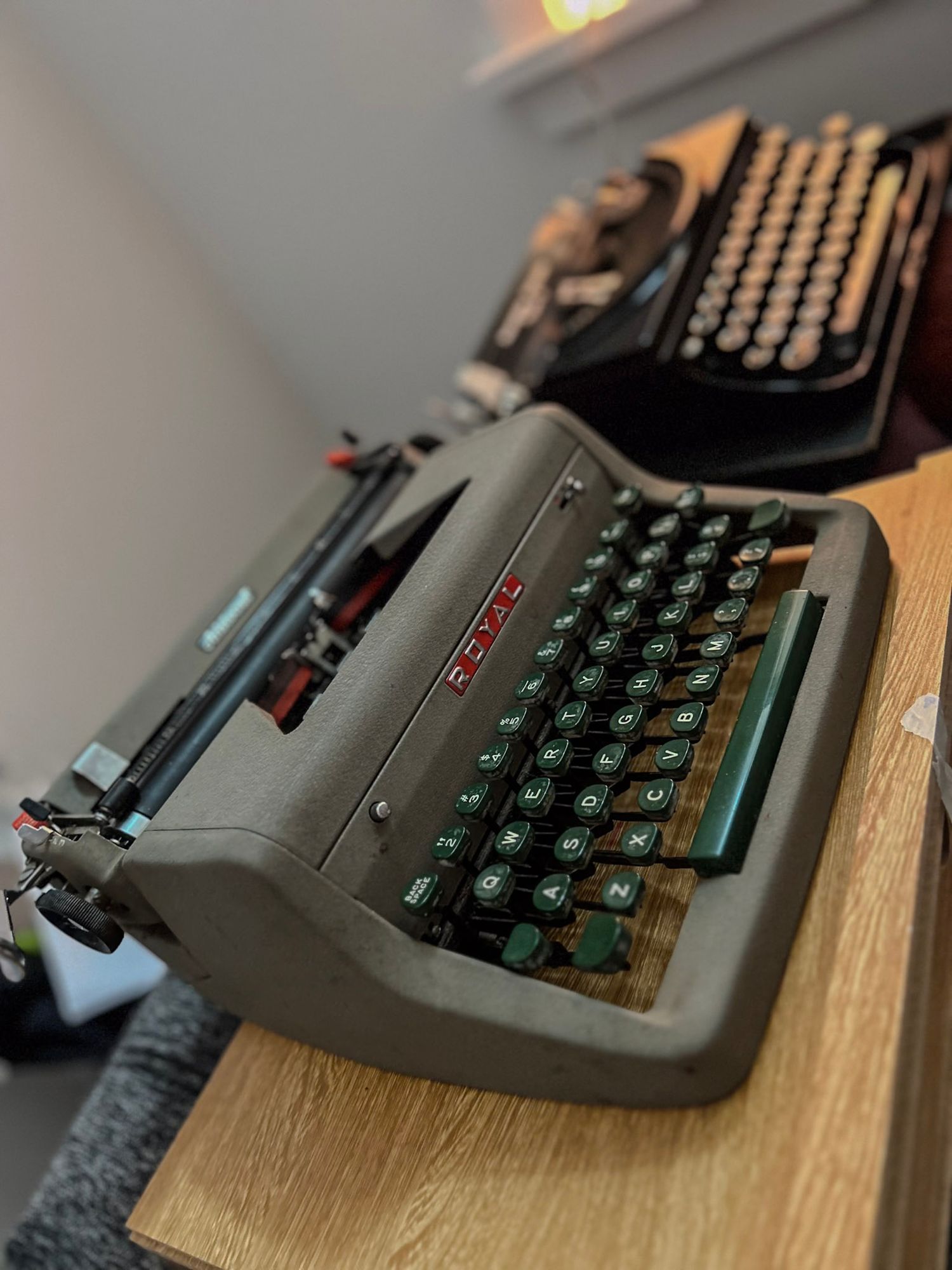 Vintage gray typewriter with green keys shown from various angles on wooden surface.