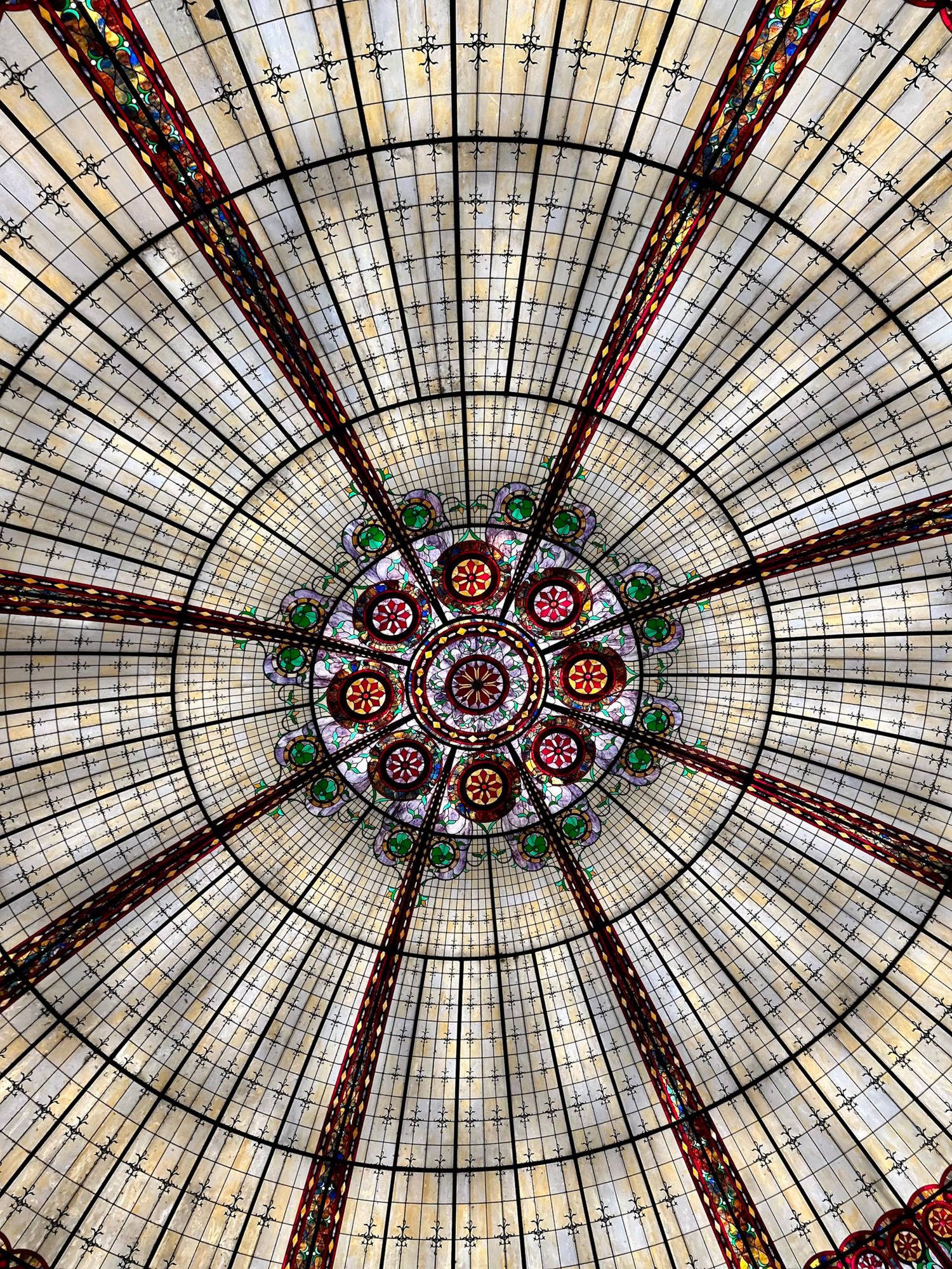 Ornate stained glass ceiling dome with intricate floral patterns and geometric designs in red, white and blue colors.