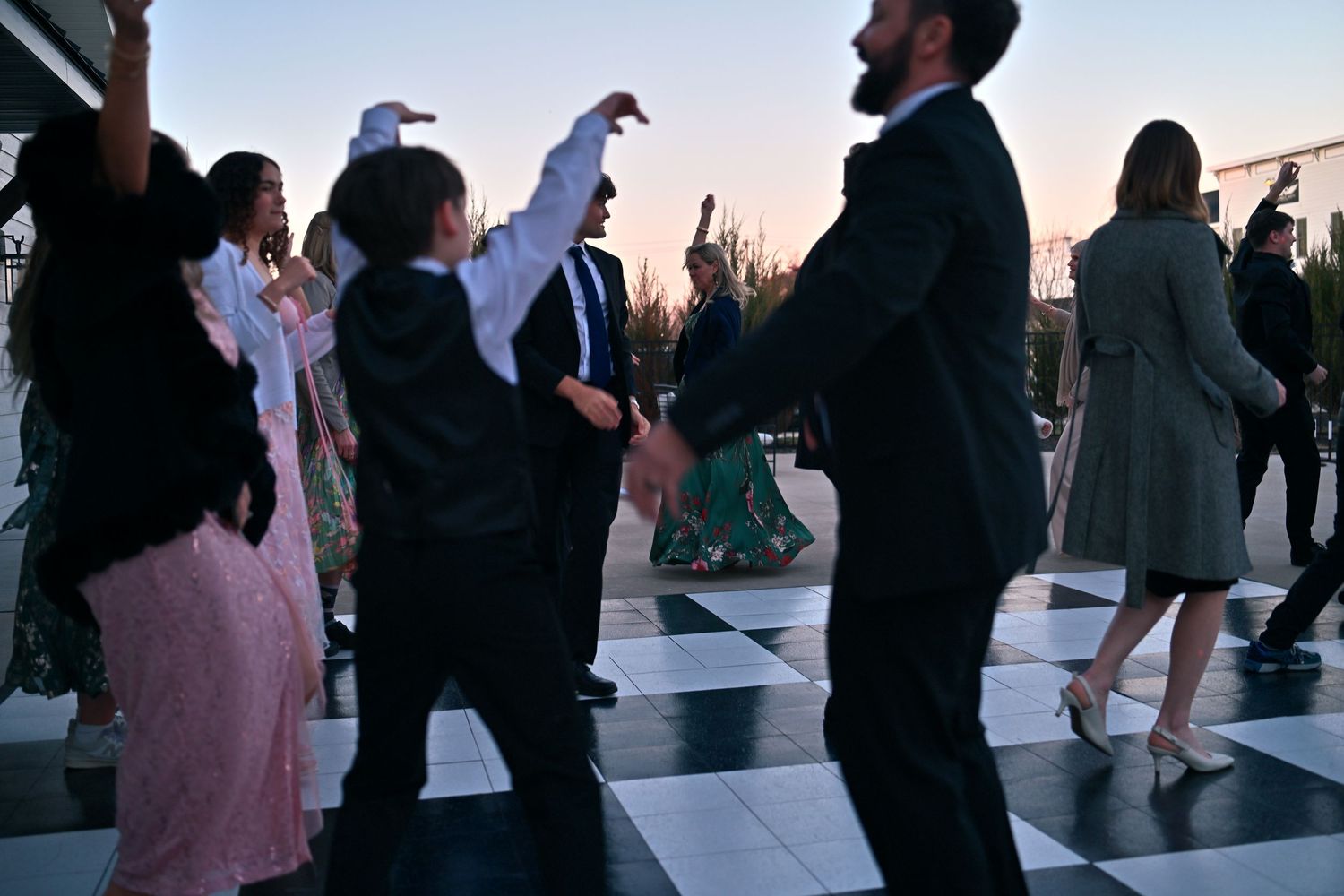 Guests dancing outdoors on a checkered dance floor at a wedding reception during sunset.
