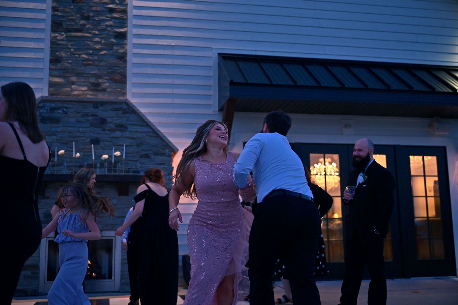 Guests dancing outdoors at an evening wedding reception near a stone building with warm glowing lights.