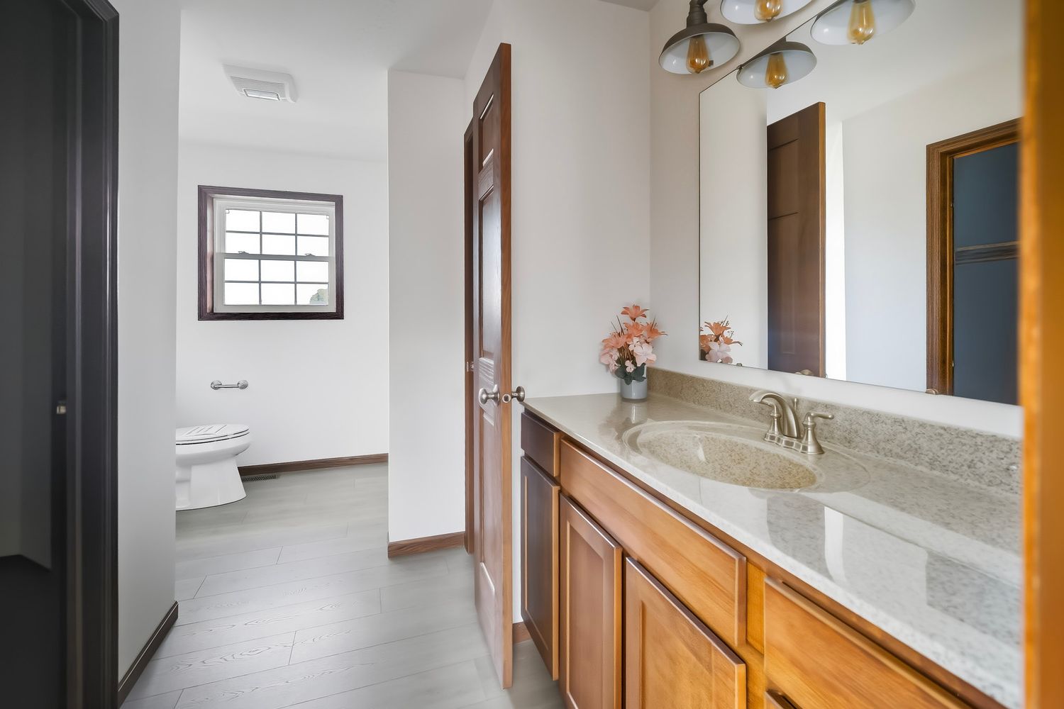 Modern bathroom interior with white walls, wooden trim, and marble-look countertops featuring a sleek vanity design.