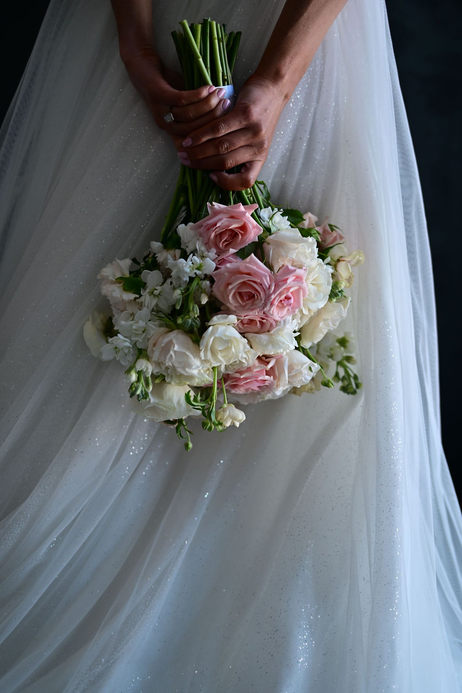 Close-up view of a delicate bridal bouquet with pink and white roses against flowing white wedding dress fabric.