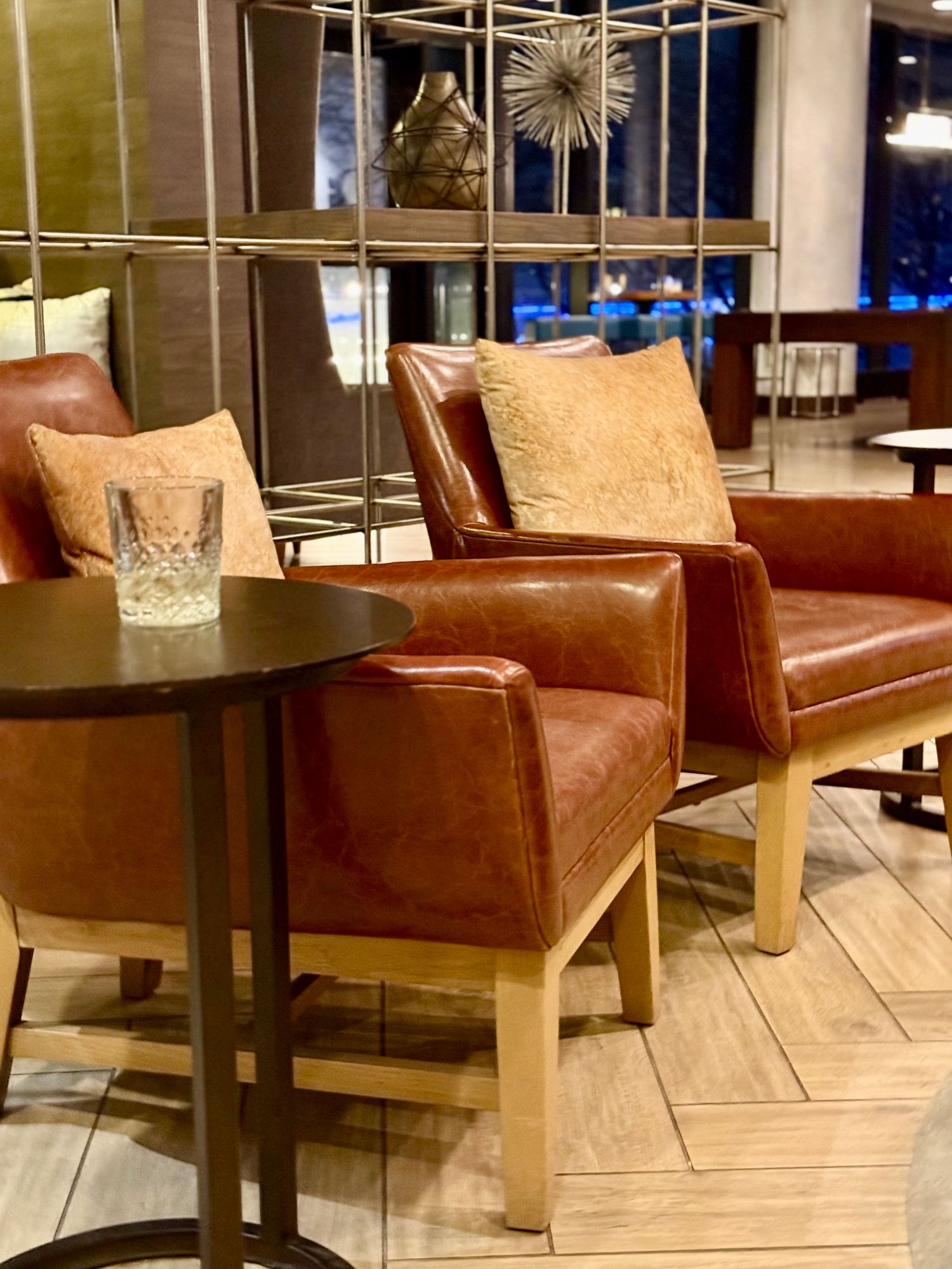 Modern lounge area with brown leather chairs, round side table, and decorative starburst light fixture in contemporary setting.
