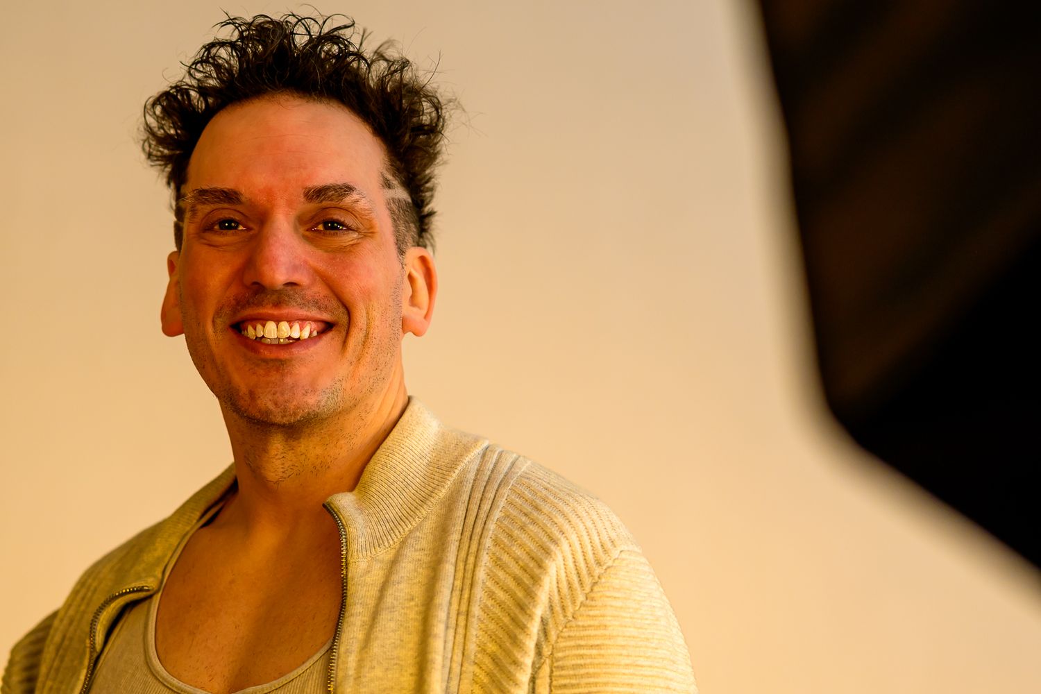A person in a cream-colored sweater smiles warmly against a beige background.