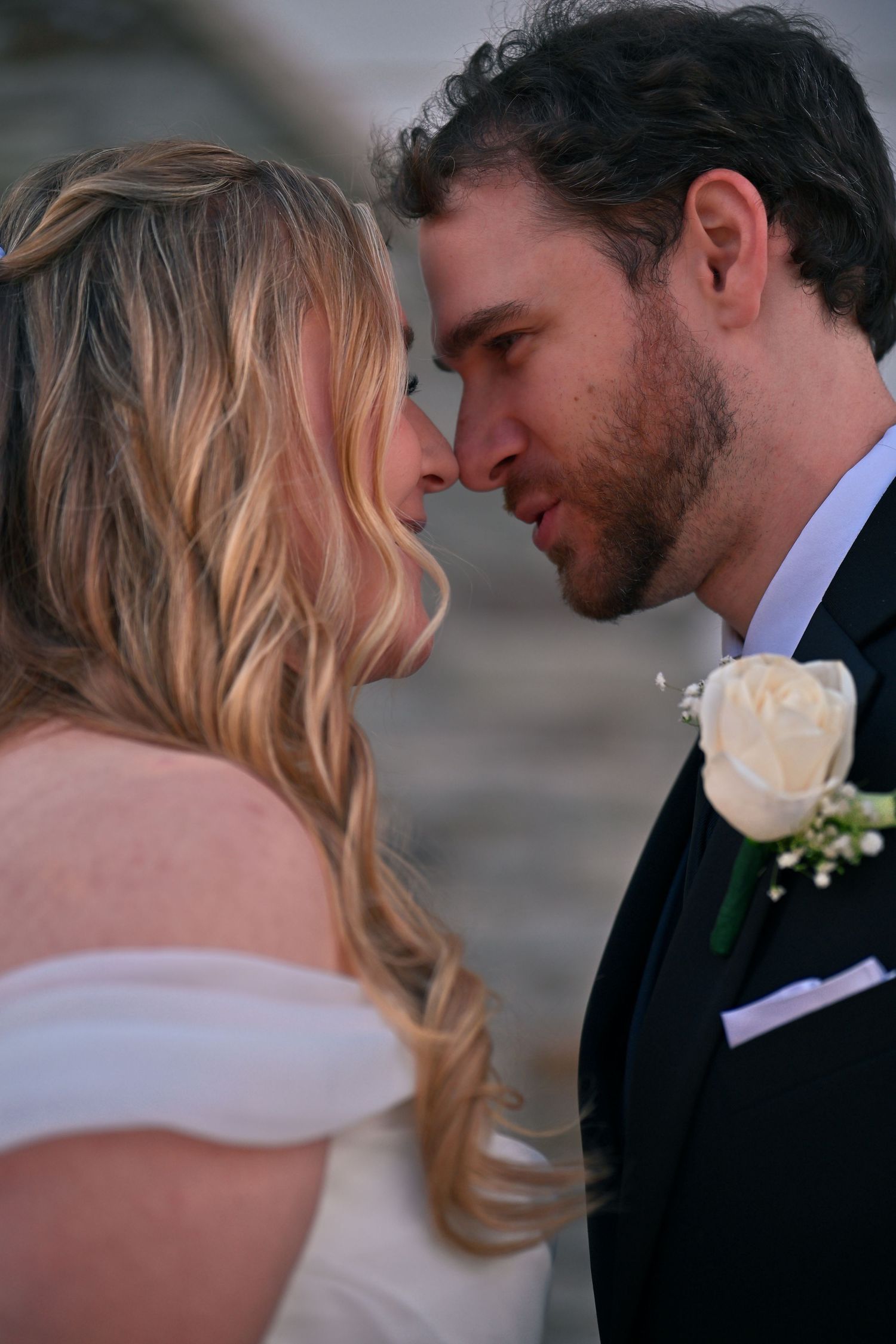 A bride and groom share an intimate moment, touching foreheads, as the groom wears a white rose boutonniere.