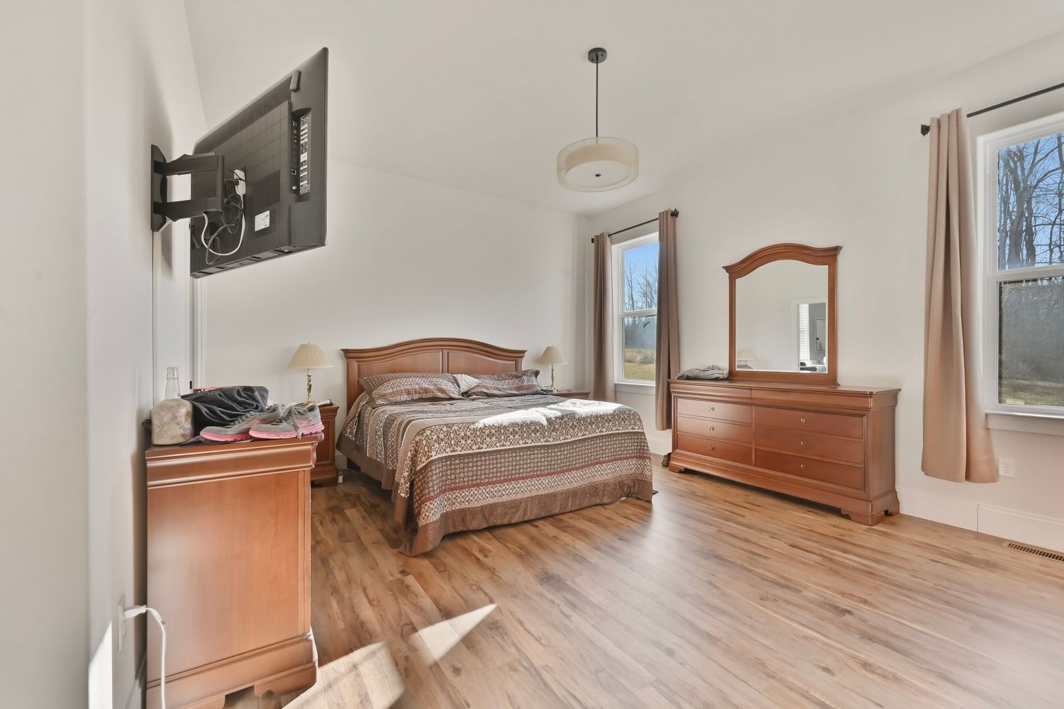 A bright, modern bedroom with hardwood floors, white walls, and natural light streaming through multiple windows.