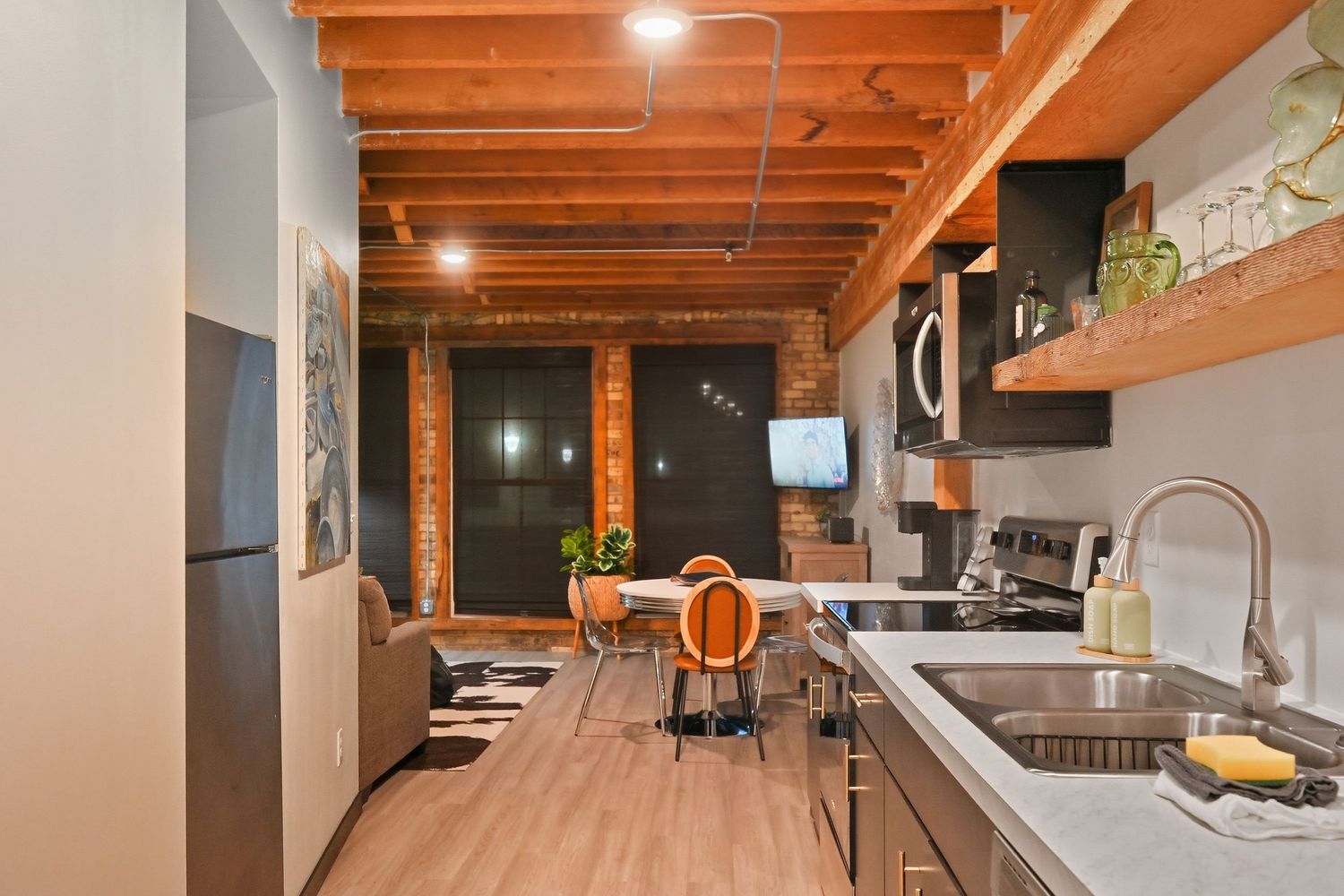 Modern basement with exposed wood ceiling beams and recessed lighting illuminating a sleek white kitchen area.