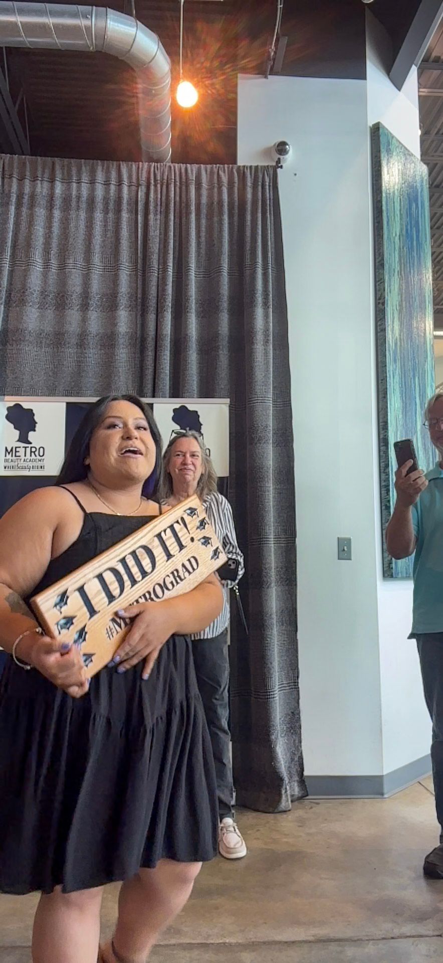 A person celebrates with an 'I DID IT!' sign at a Metro graduation event.