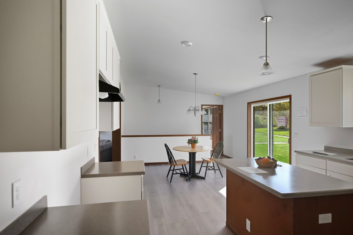Bright open concept living space with white walls, light hardwood floors and pendant lighting fixtures.