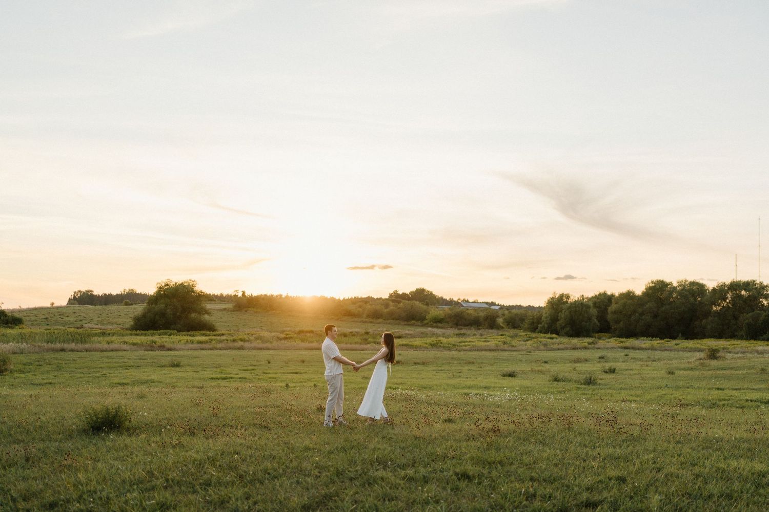 A future Bride and Groom holding hands in a golden sunset field on their wedding day in a scenic countryside.
