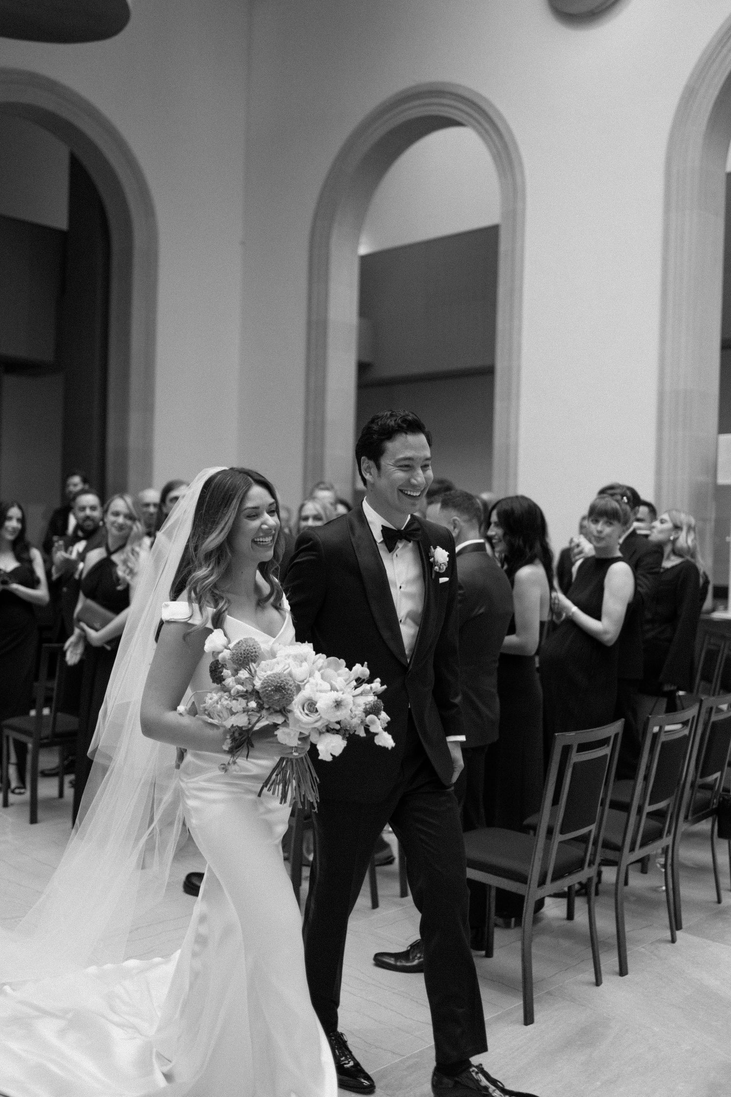 Black and white photo of a joyful bride and groom walking back down the aisle after their ceremony.