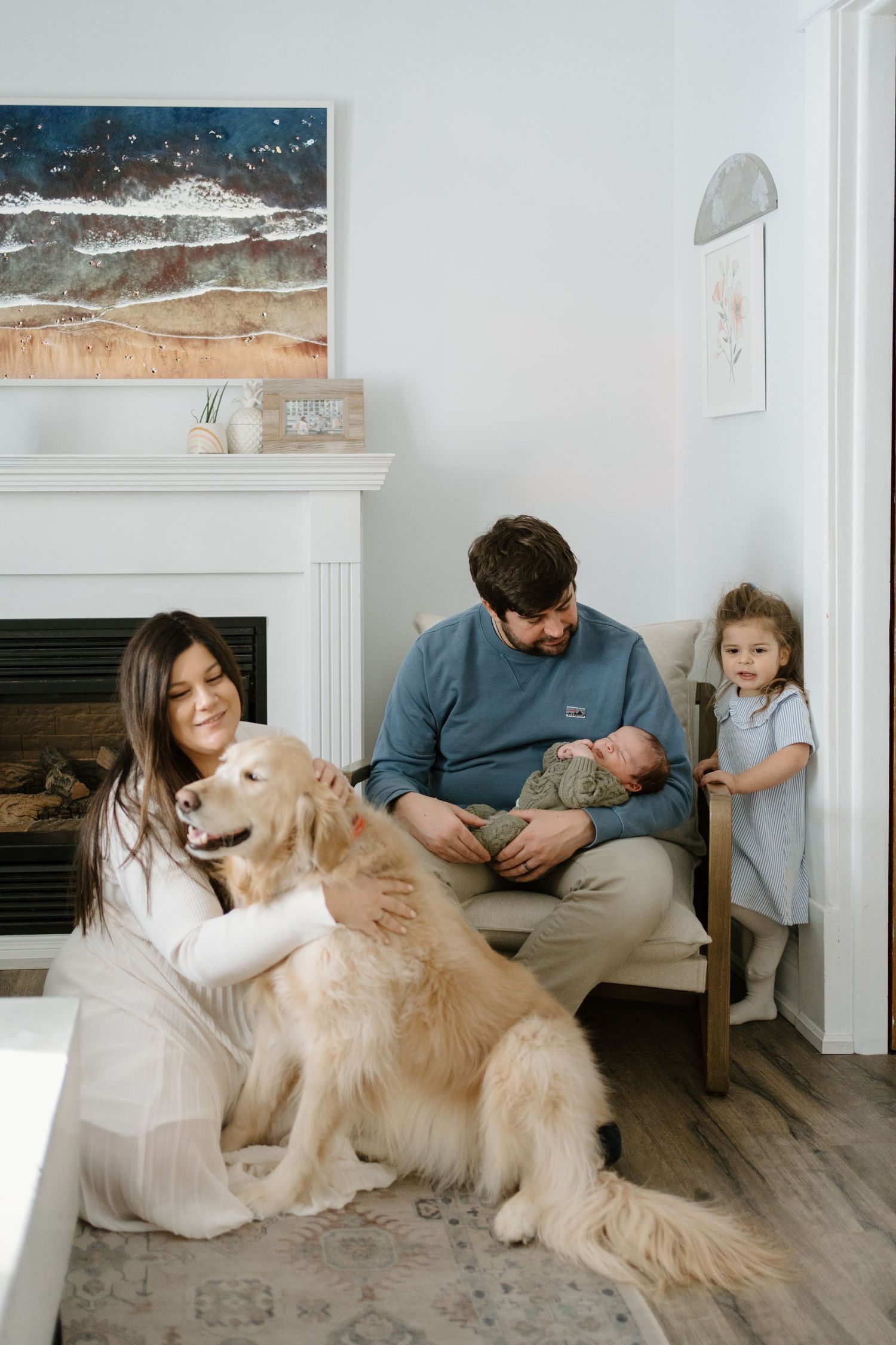 Happy family with golden retriever, newborn baby, and toddler posing near fireplace indoors.