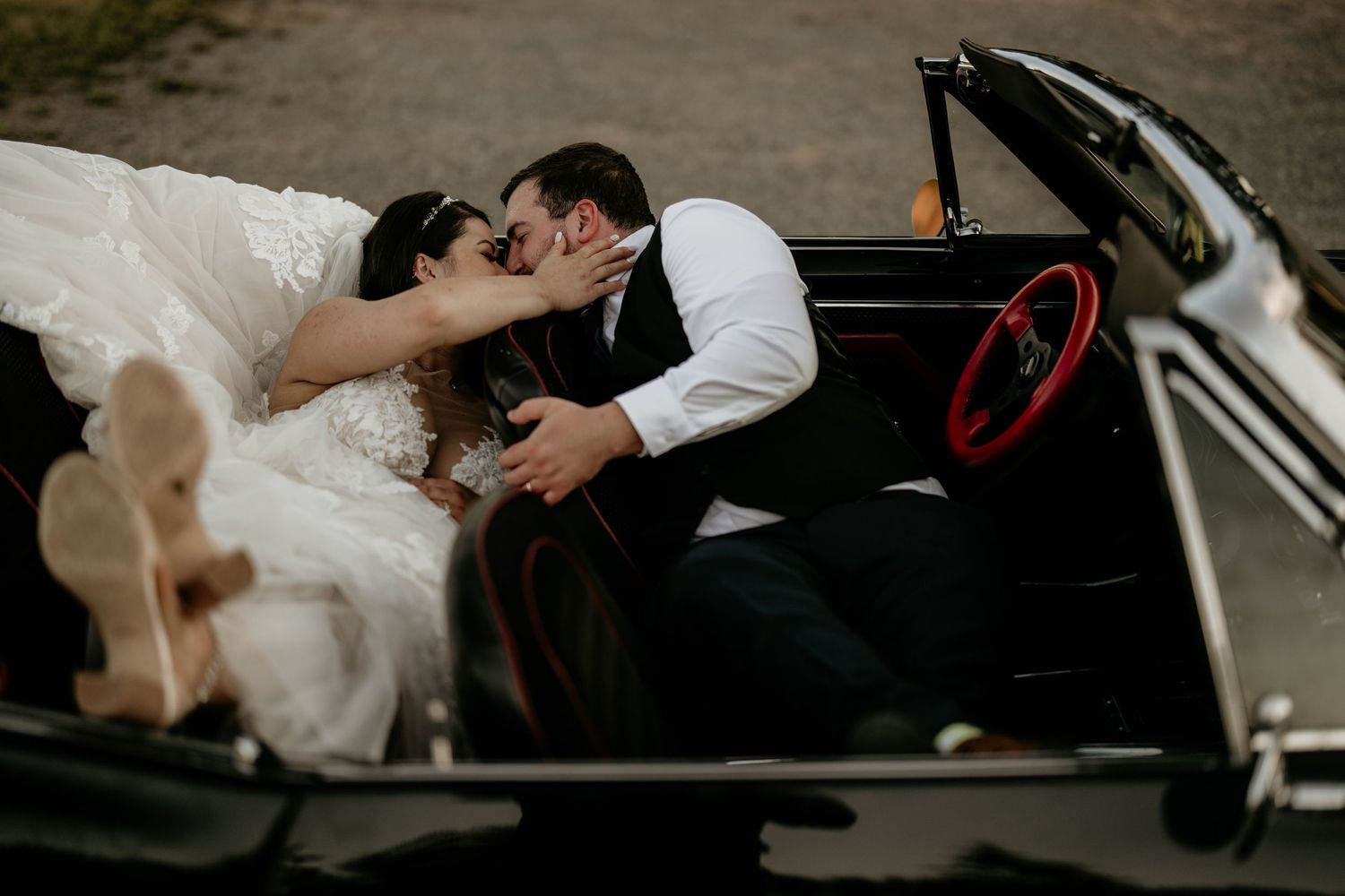A husband and wife laying in the back seat of the car kissing.